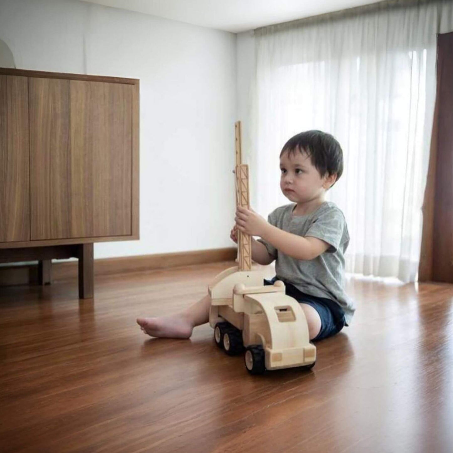 Child playing with PlanToys Fire Truck in a room with wooden flooring and a cabinet.