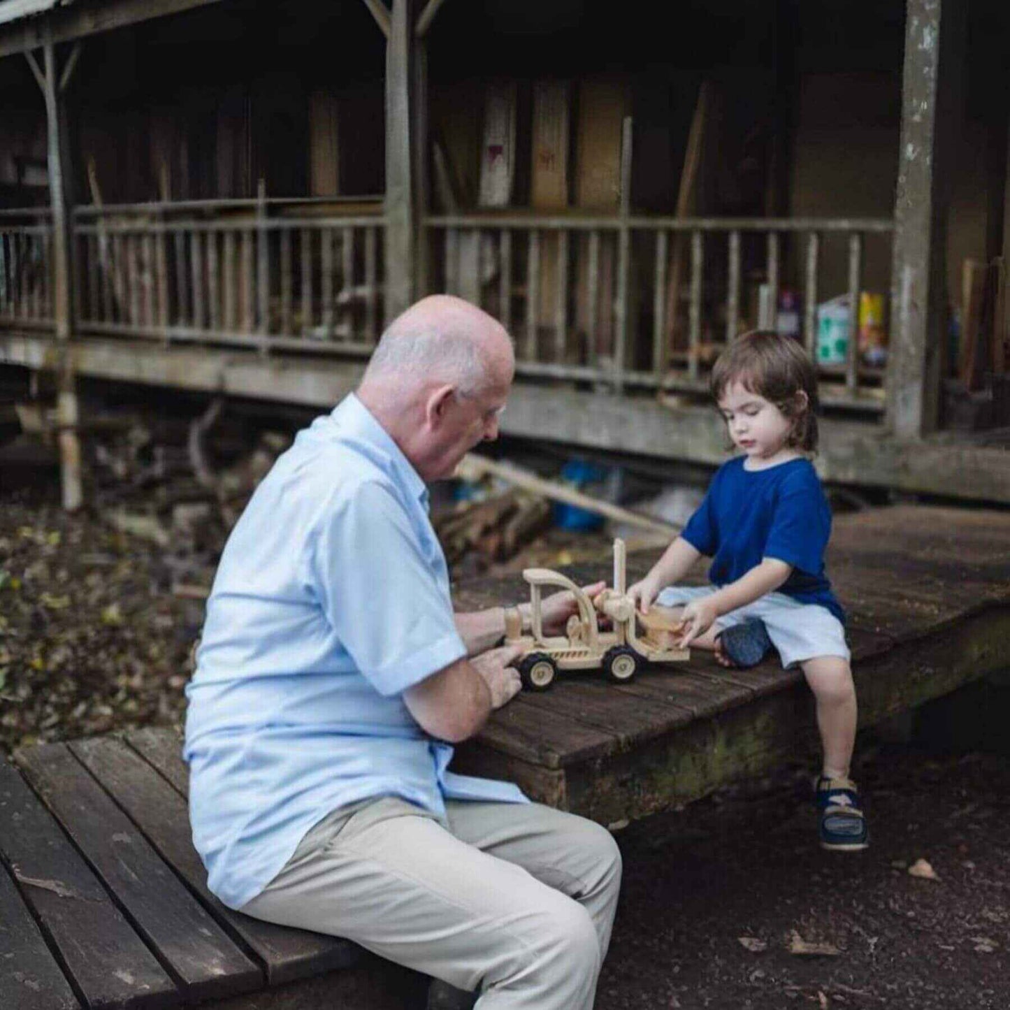 Man and child playing with PlanToys Forklift on a wooden platform.