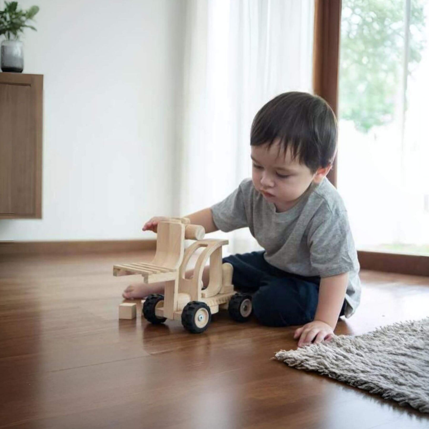 Child playing with PlanToys Forklift on a wooden floor