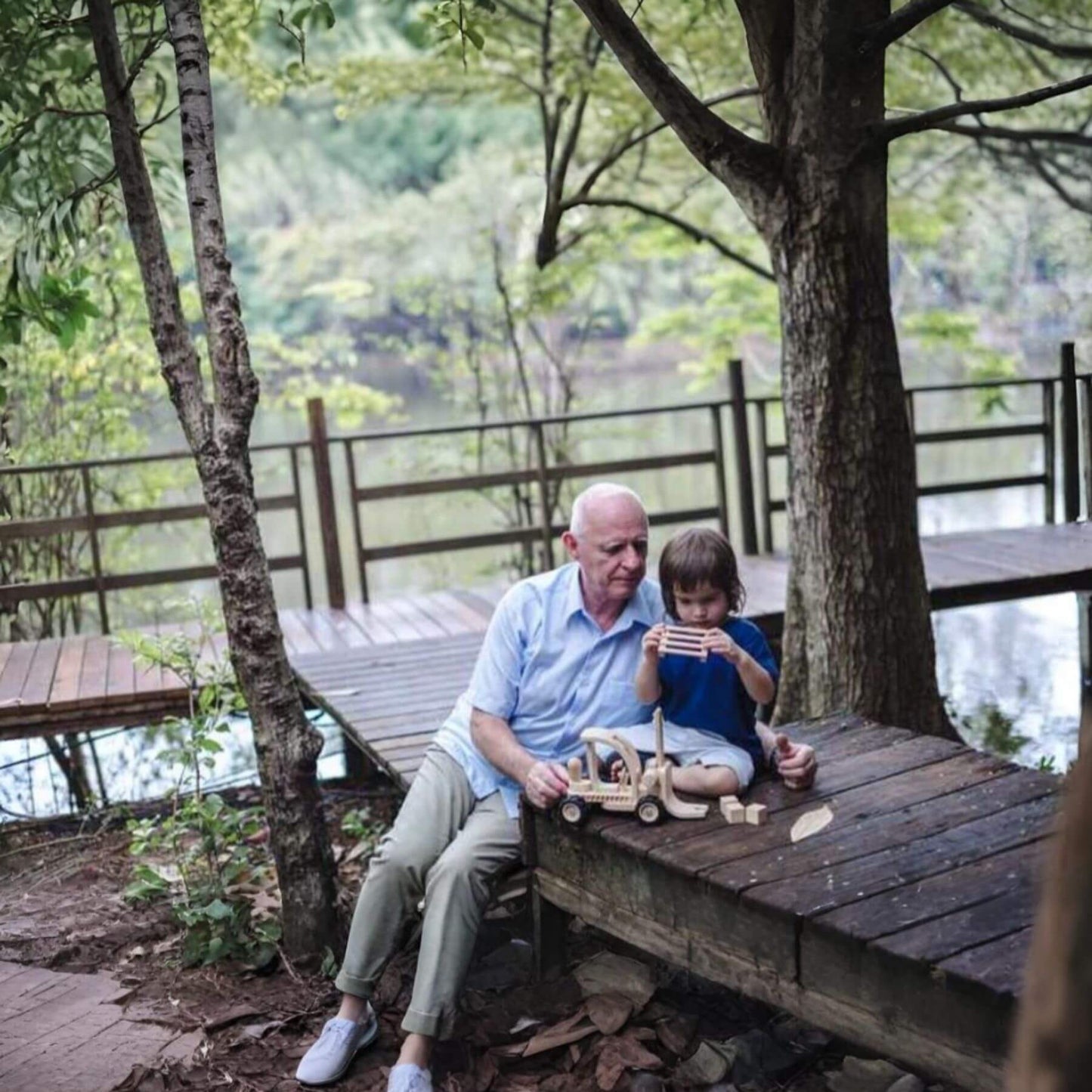 Man and child playing with PlanToys Forklift on a wooden deck with a scenic background