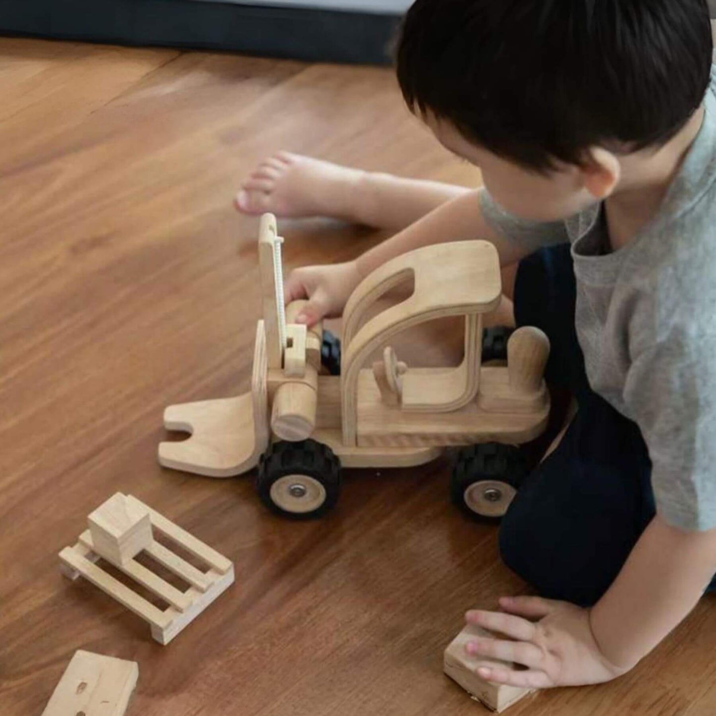 Child playing with PlanToys Forklift on a wooden floor