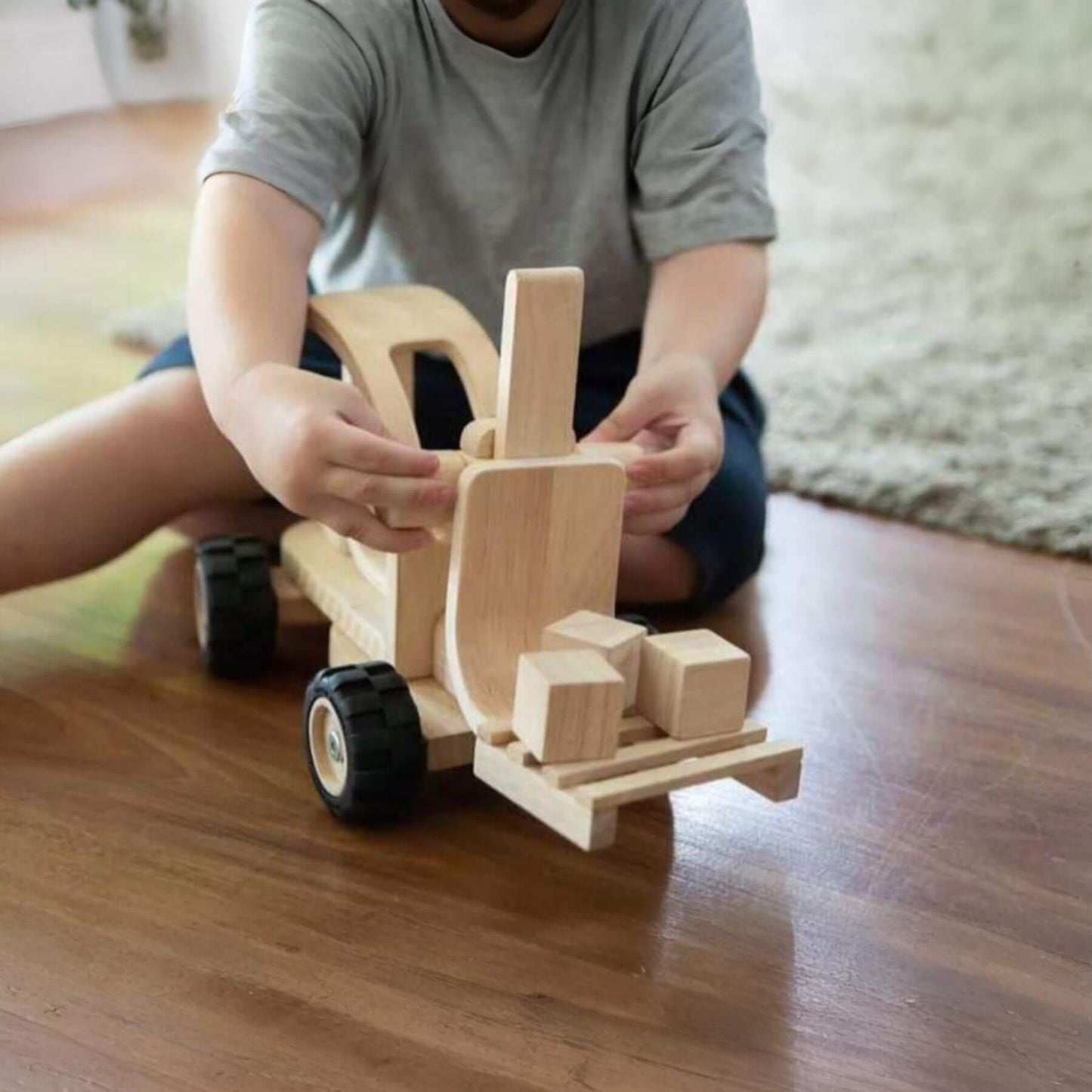 Child playing with PlanToys Forklift on a wooden floor.