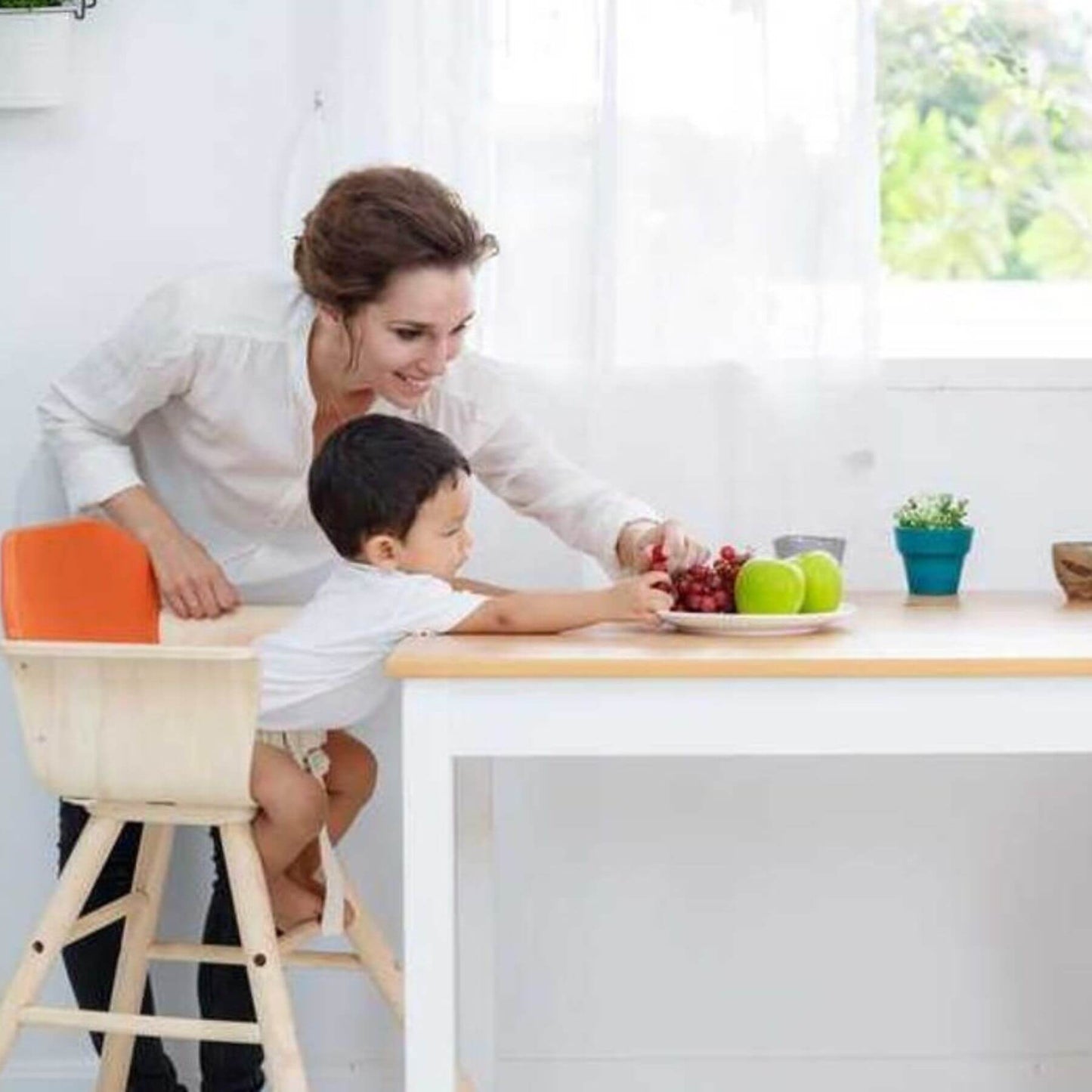 Woman and child sitting on PlanToys High Chair - Orange, at a kitchen counter with fruits