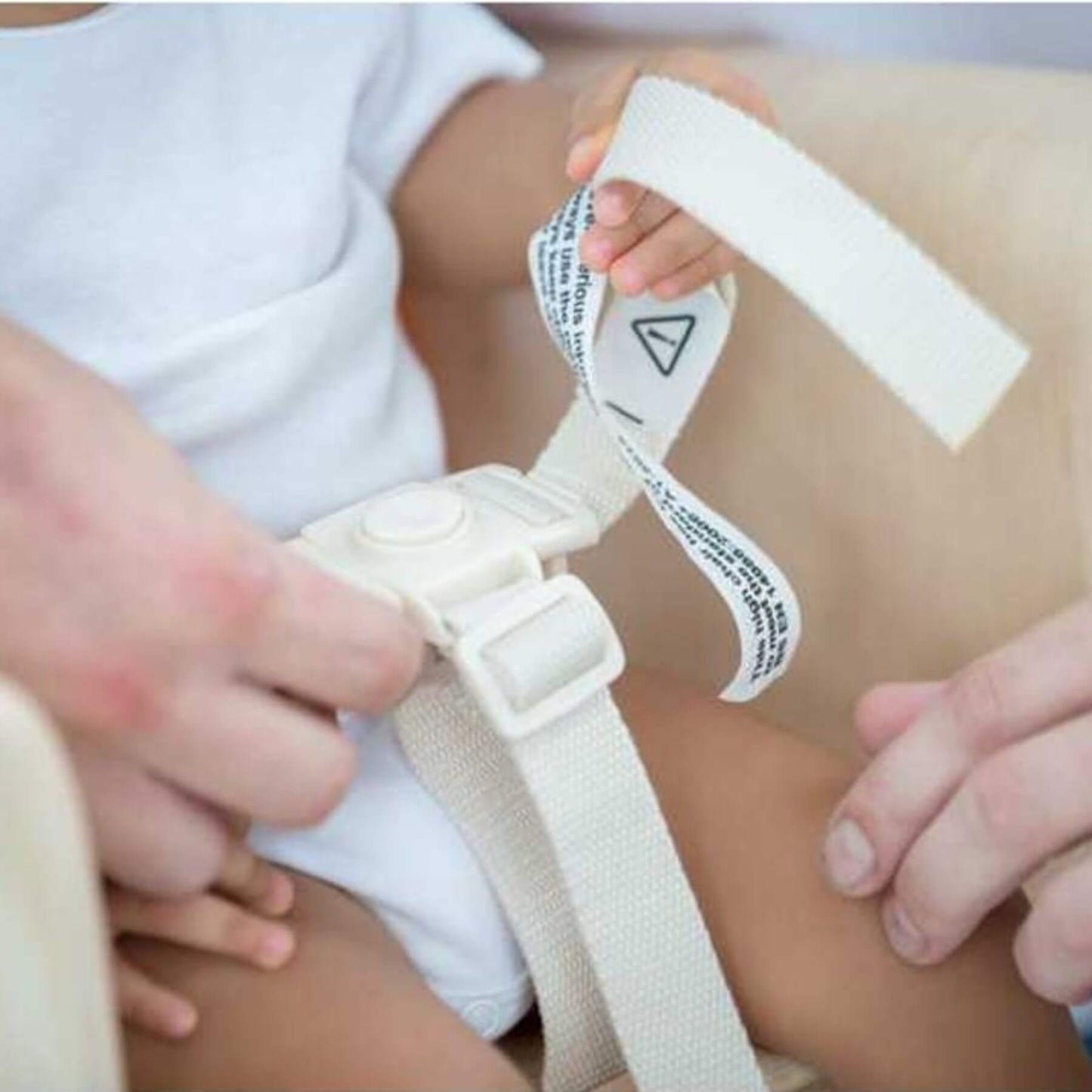 Close-up of a baby sitting on PlanToys High Chair - Orange with a white strap being adjusted.