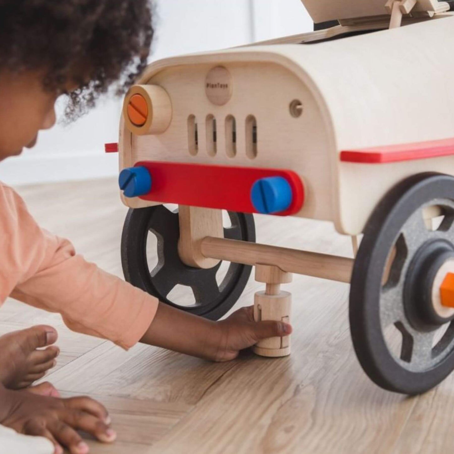 Child playing with PlanToys Motor Mechanic on a light wood floor.