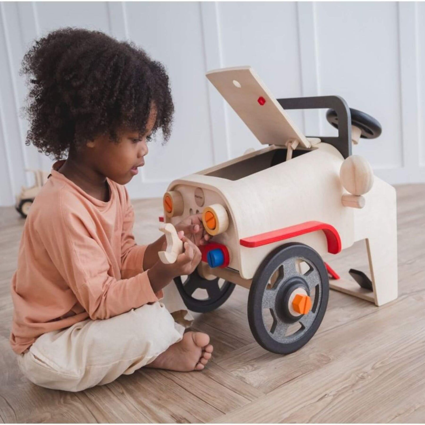 Child playing with PlanToys Motor Mechanic on a wooden floor.