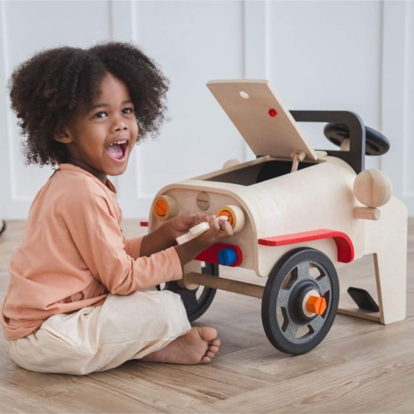 Child playing with PlanToys Motor Mechanic on a wooden floor.