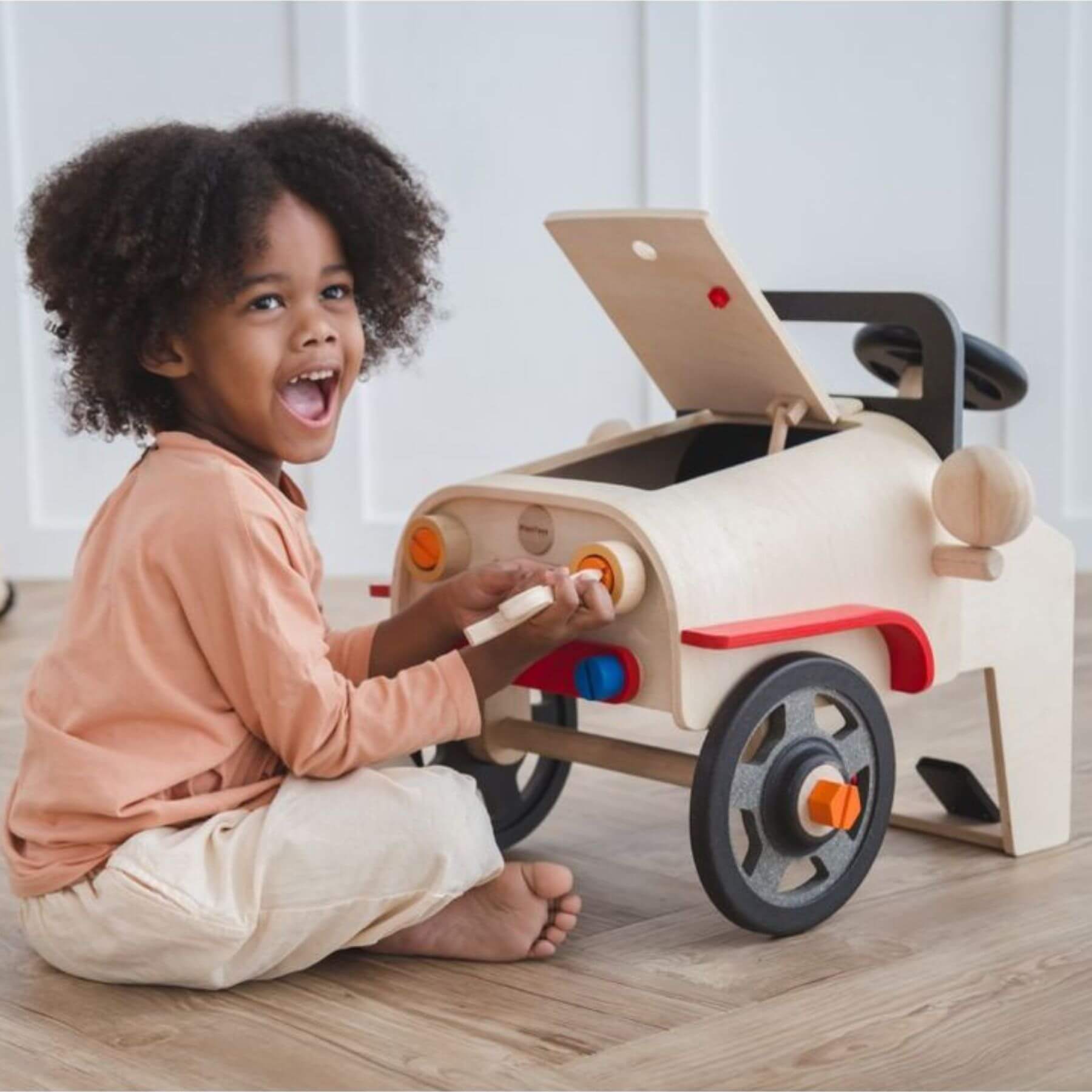 Child playing with PlanToys Motor Mechanic on a wooden floor.