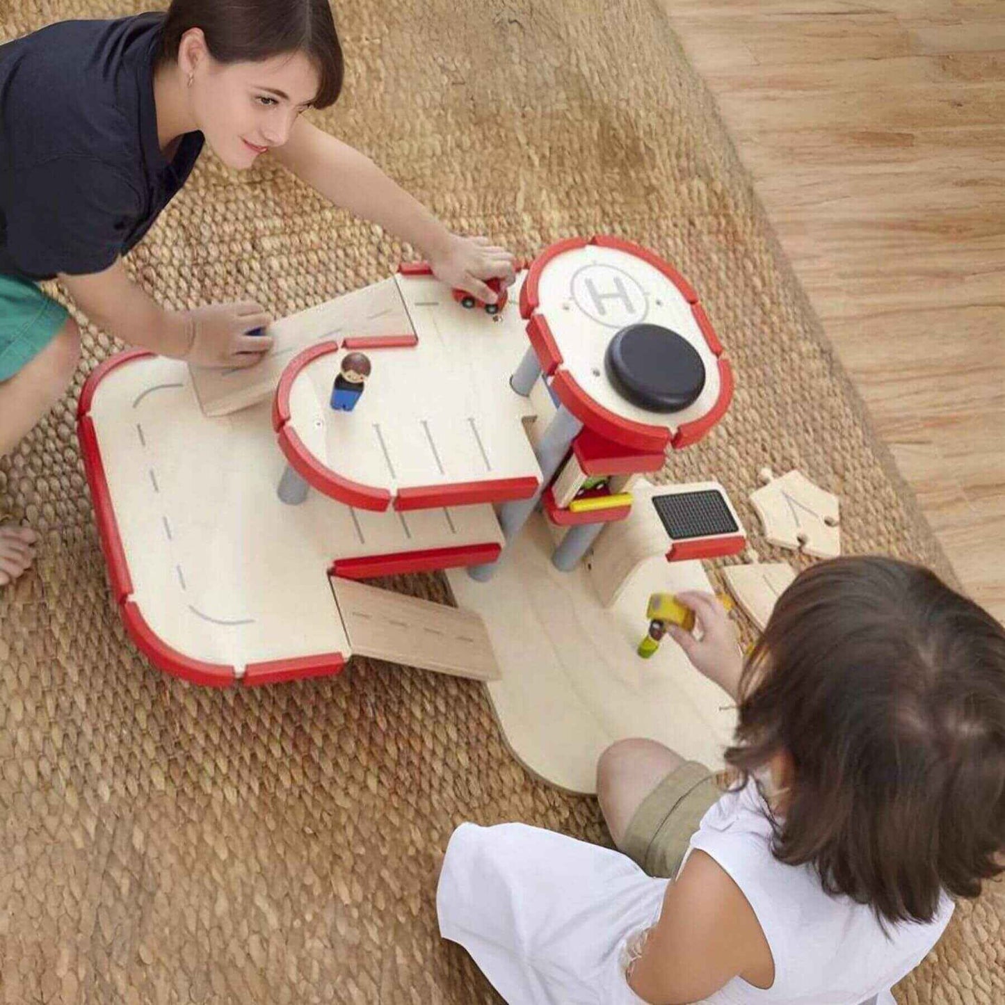 Two children playing with PlanToys Parking Garage on a wooden floor.