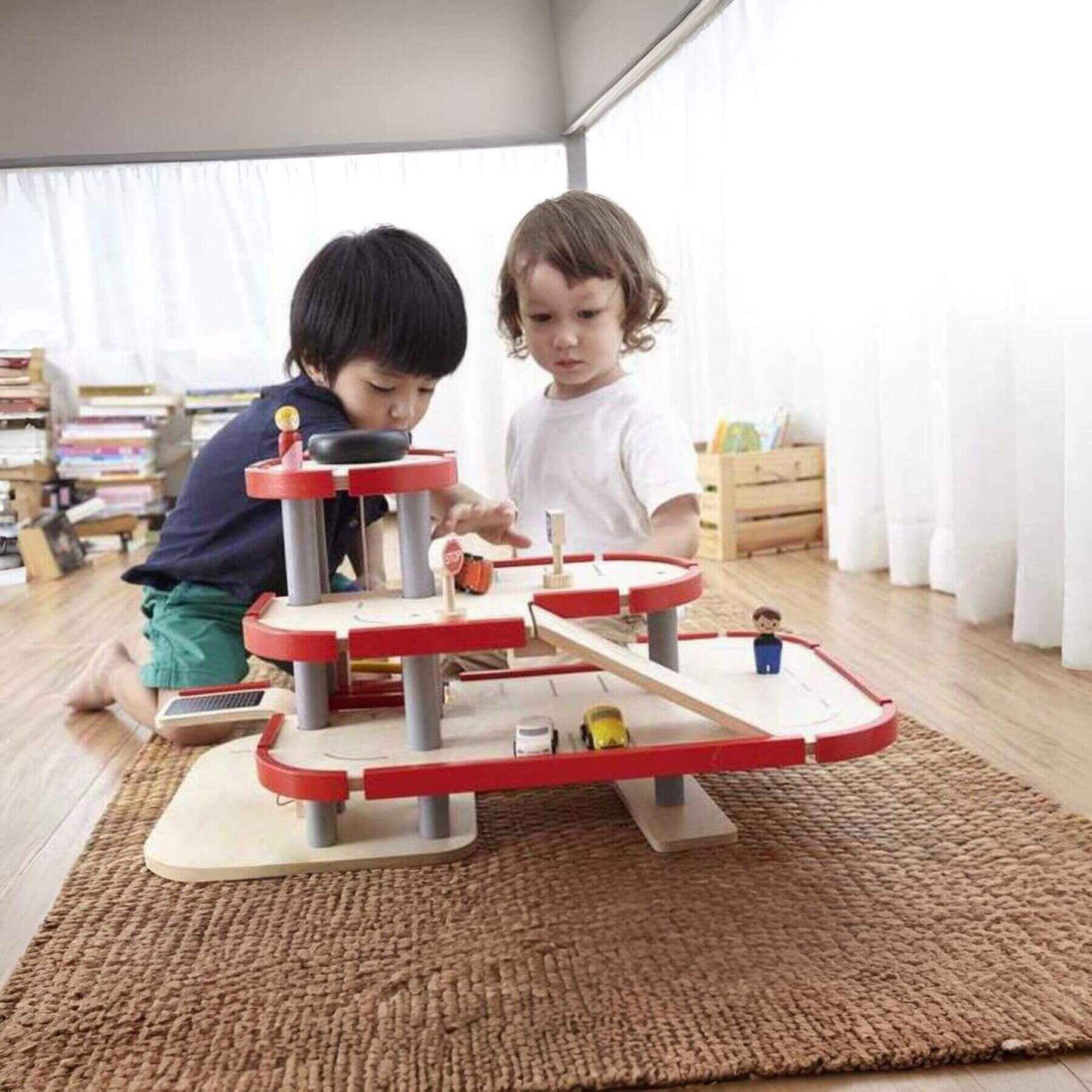 Two children playing with PlanToys Parking Garage on a rug in a room.