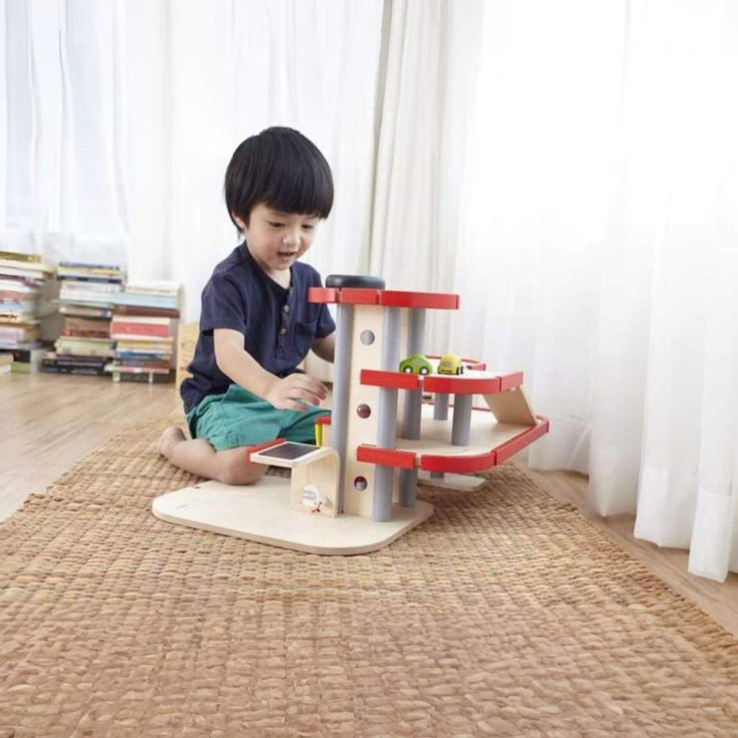 Child playing with PlanToys Parking Garage in a room with books and curtains.
