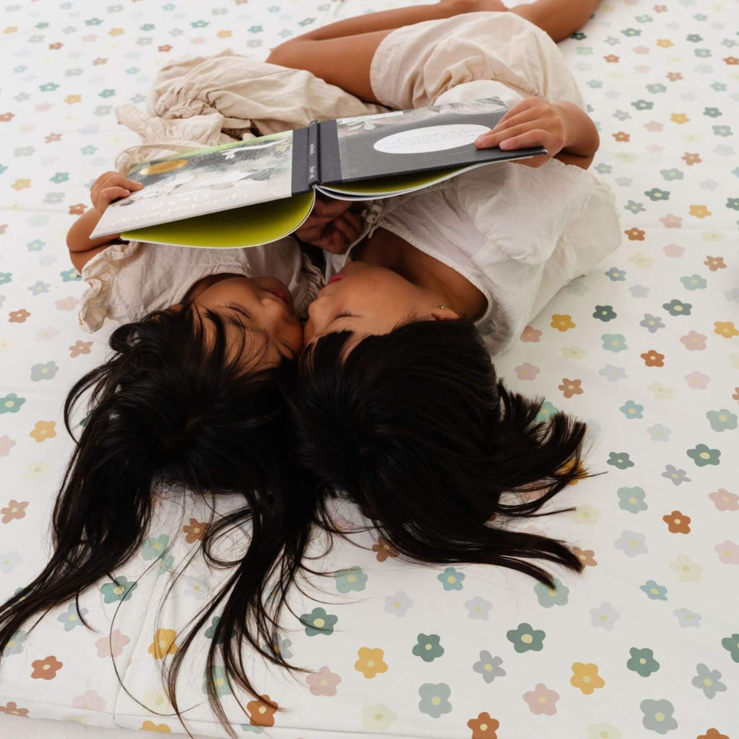 Two people lying on Toki Kids Playful Posies Vegan Leather Mat, one of them reading a book.