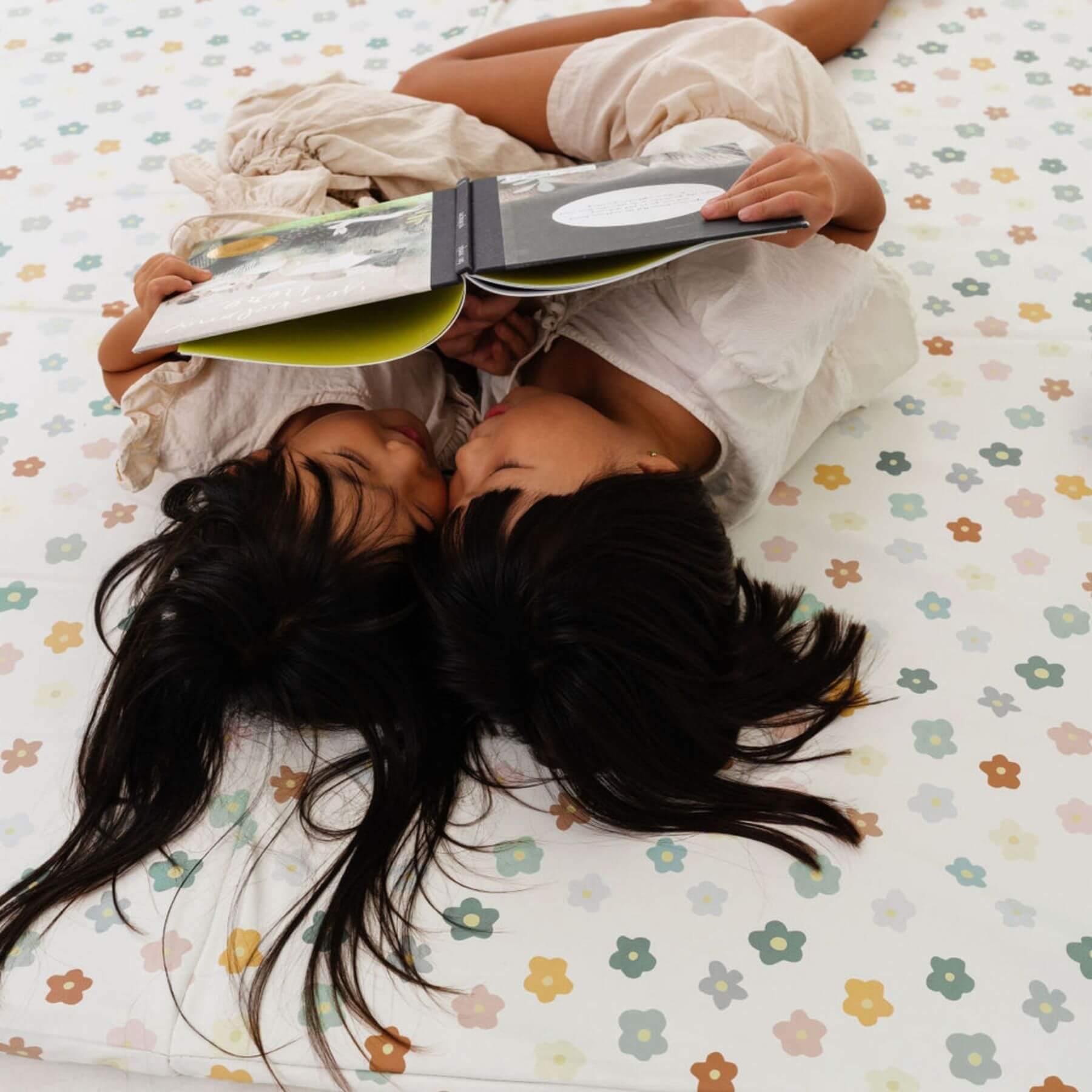 Two people lying on Toki Kids Playful Posies Vegan Leather Mat, one of them reading a book.