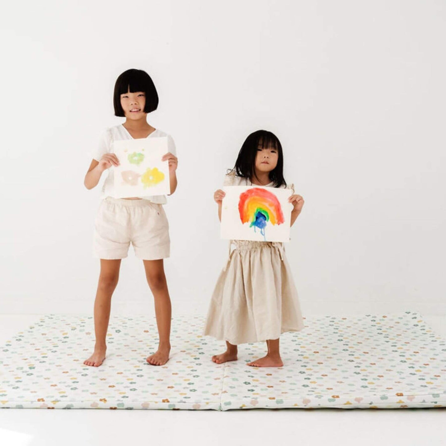 Two children holding up their colorful drawings on Toki Kids Playful Posies Vegan Leather Mat