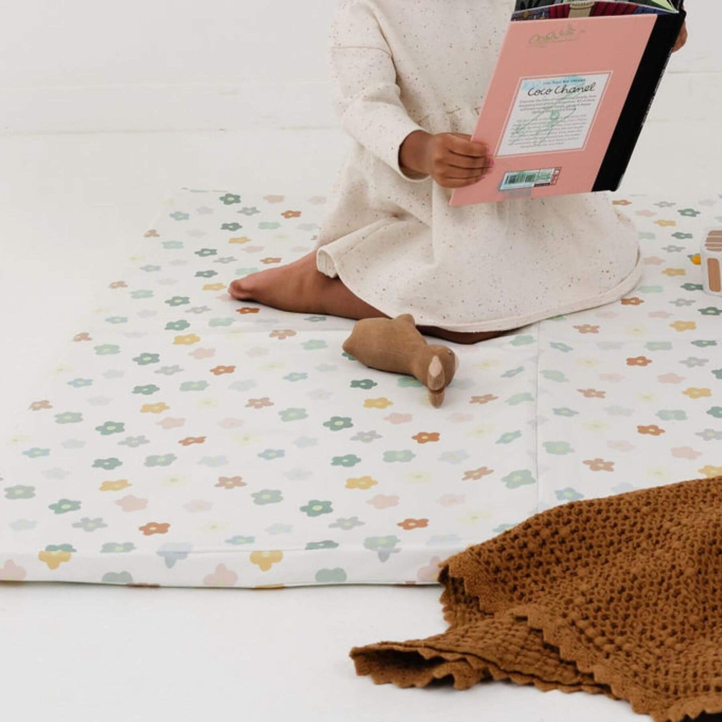Person sitting on Toki Kids Playful Posies Vegan Leather Mat reading a book with a brown blanket beside them.