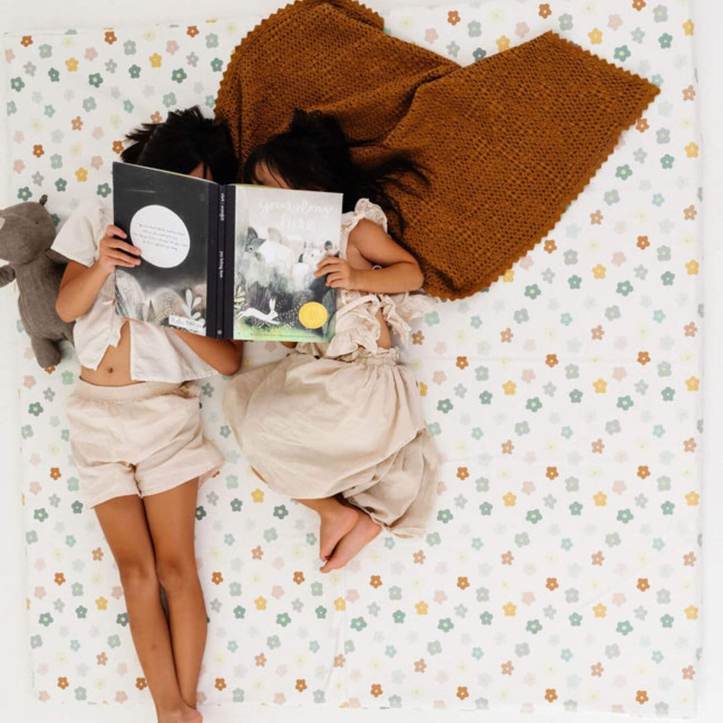 Two children lying on Toki Kids Playful Posies Vegan Leather Mat, one reading a book.