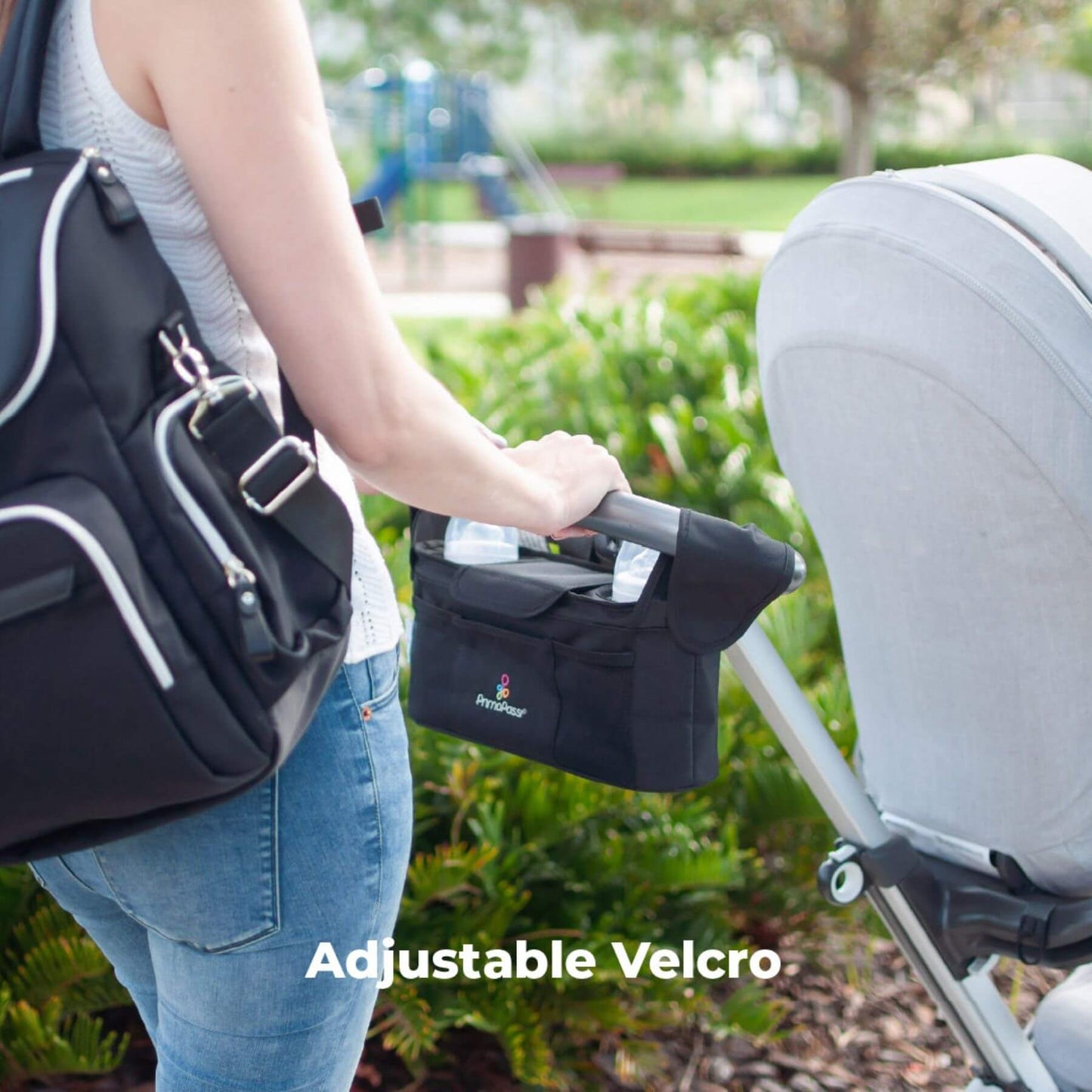 Person holding a black stroller with Stroller Handle Organizer, standing next to a stroller in an outdoor setting.