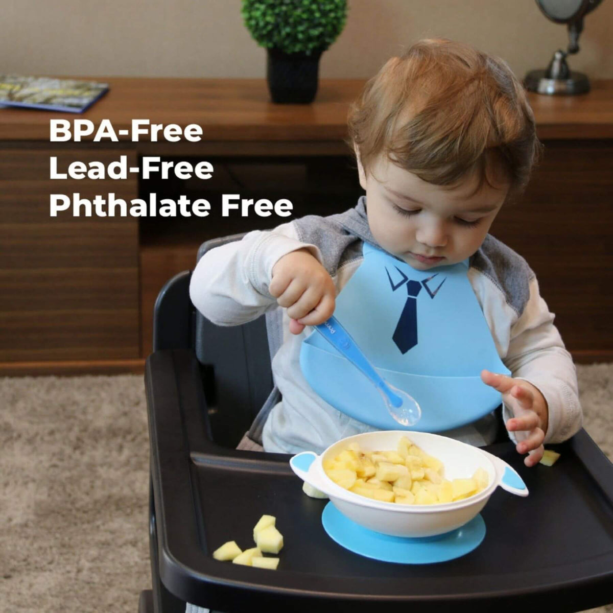 A toddler sitting in a high chair wearing Primo Passi Silicone Baby Bib - Blue Tie, eating from a white bowl with a blue handle and matching blue suction cup on a black tray. The image features text overlays reading 'BPA-Free Lead-Free Phthalate Free'.