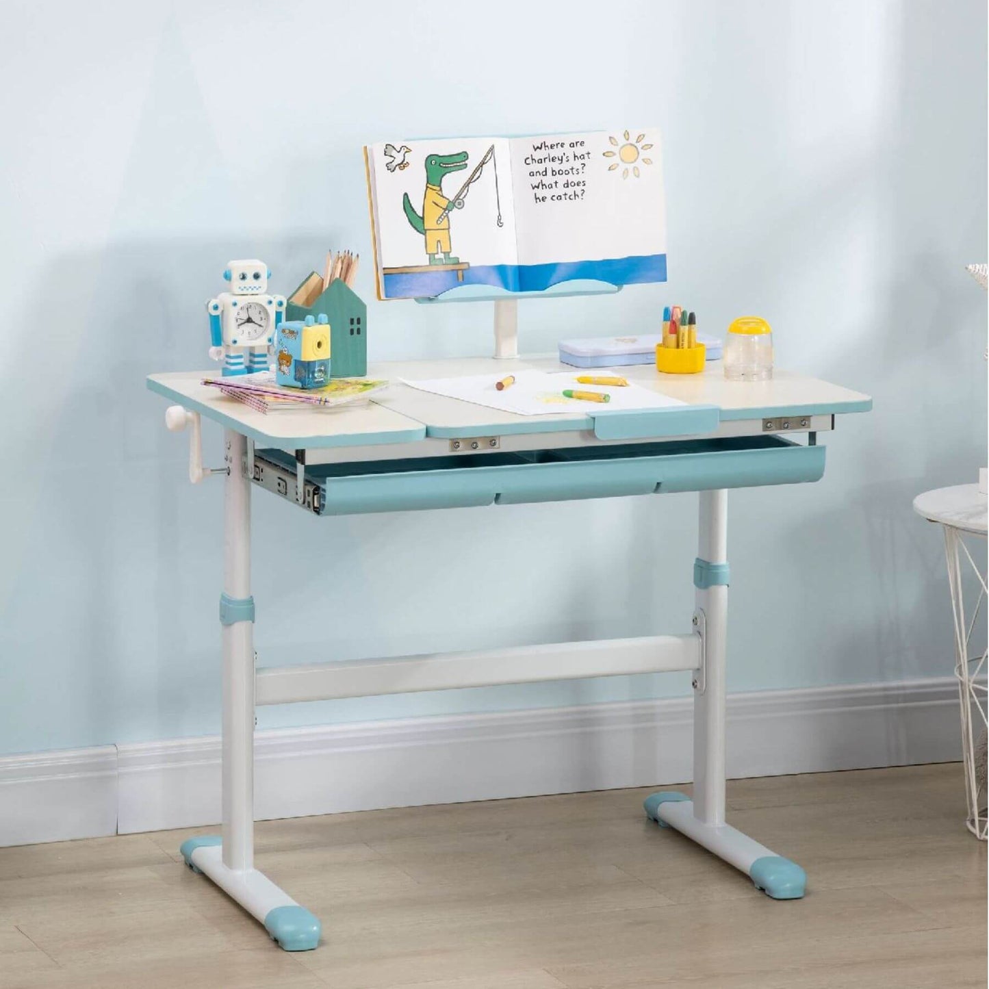 Qaba Height Adjustable Children School Study Table with Tilt Desktop Blue with various stationery items against a light blue wall.