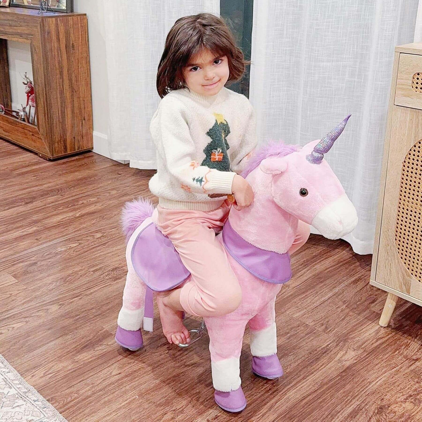 Child riding Qaba Ride On Real Walking Unicorn with Sparkly Horn Pink on a wooden floor.