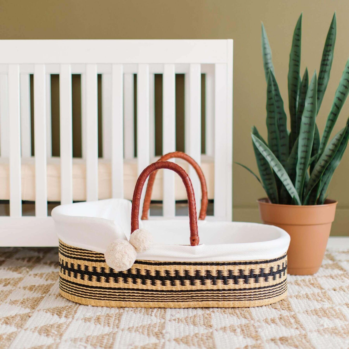 Plum+Sparrow Remy African Moses Basket on a checkered floor in front of a white crib.