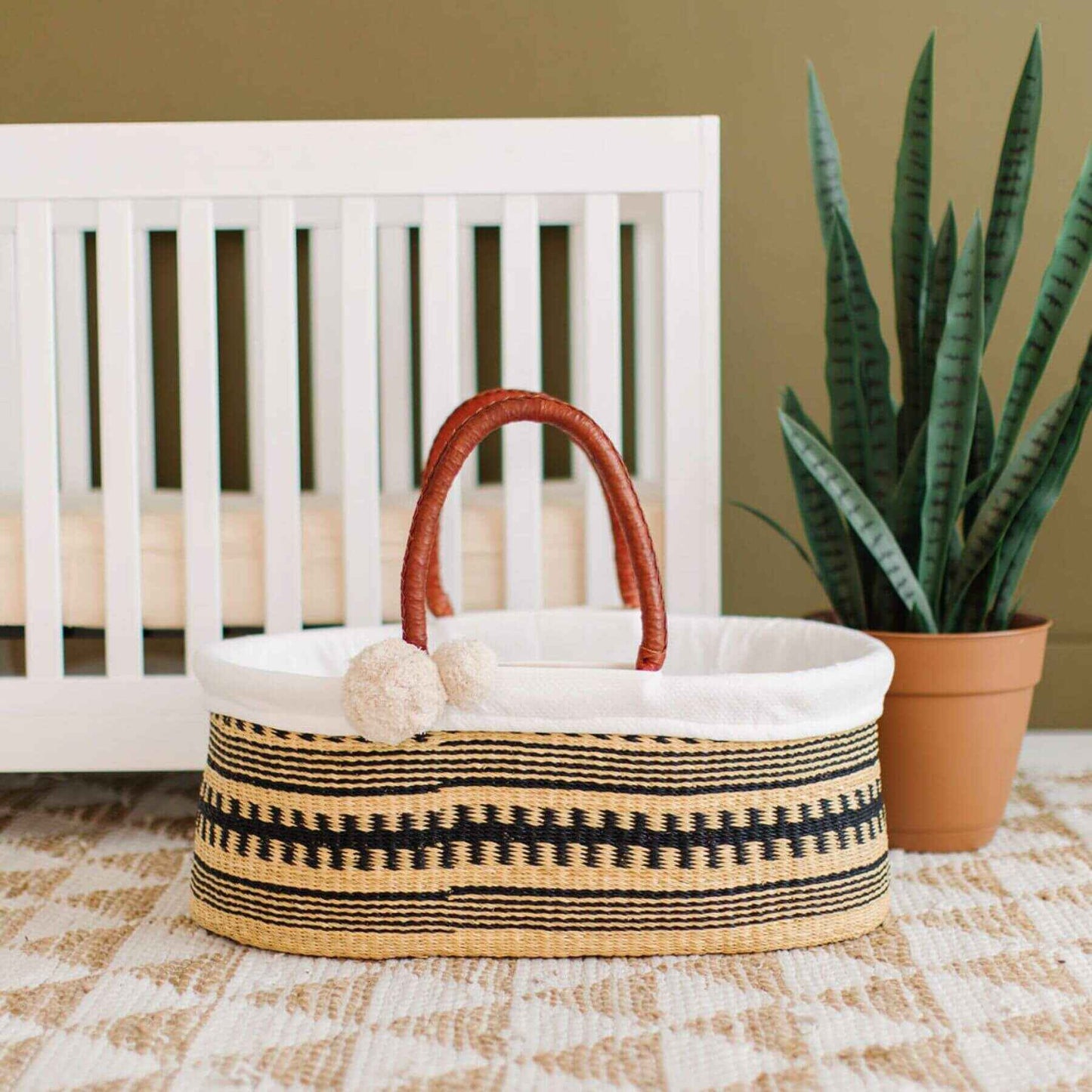 Plum+Sparrow Remy No Hood African Moses Basket in a room with a crib and plant