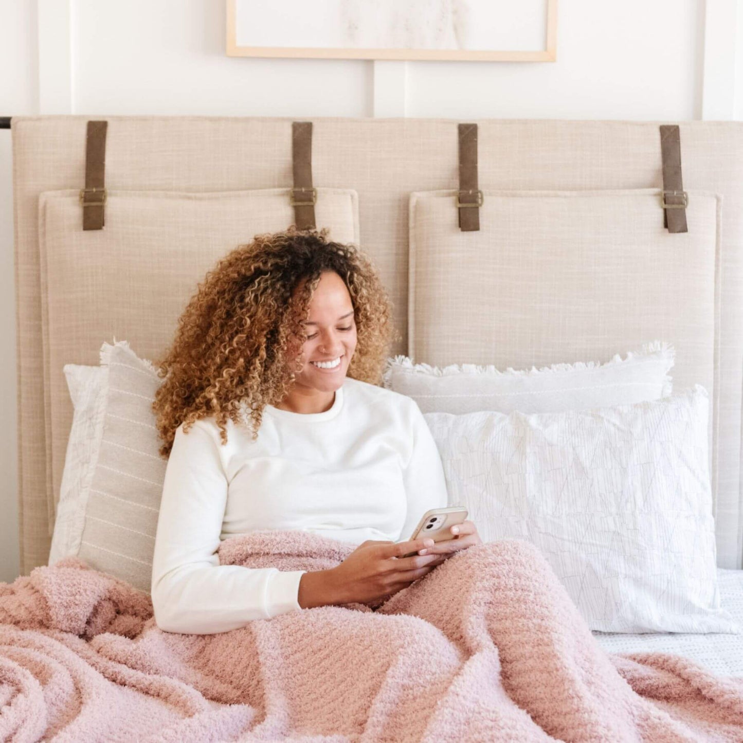 Woman sitting on a bed using a phone, wrapped in Ribbed Bamboni® Throw Blankets Cameo