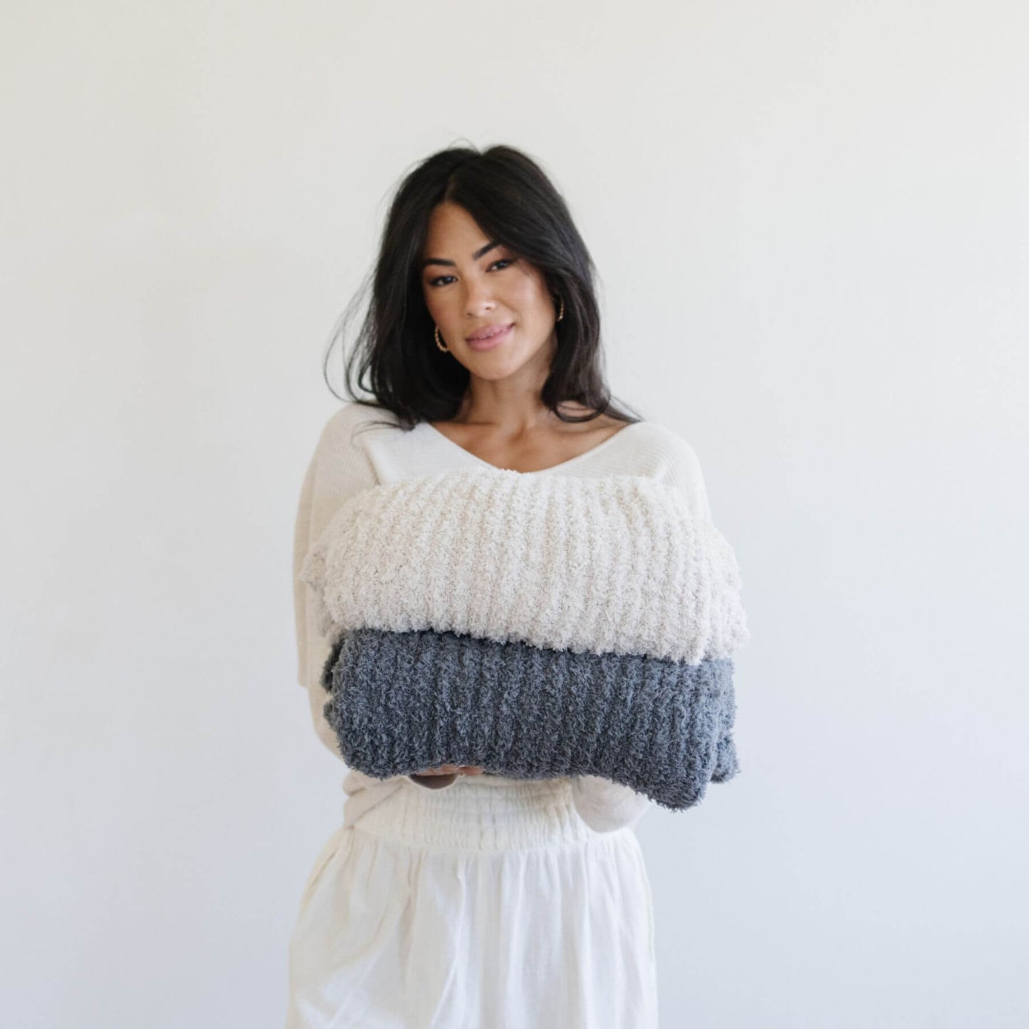 Woman wearing a sweater, holding two Ribbed Bamboni® Throw Blankets