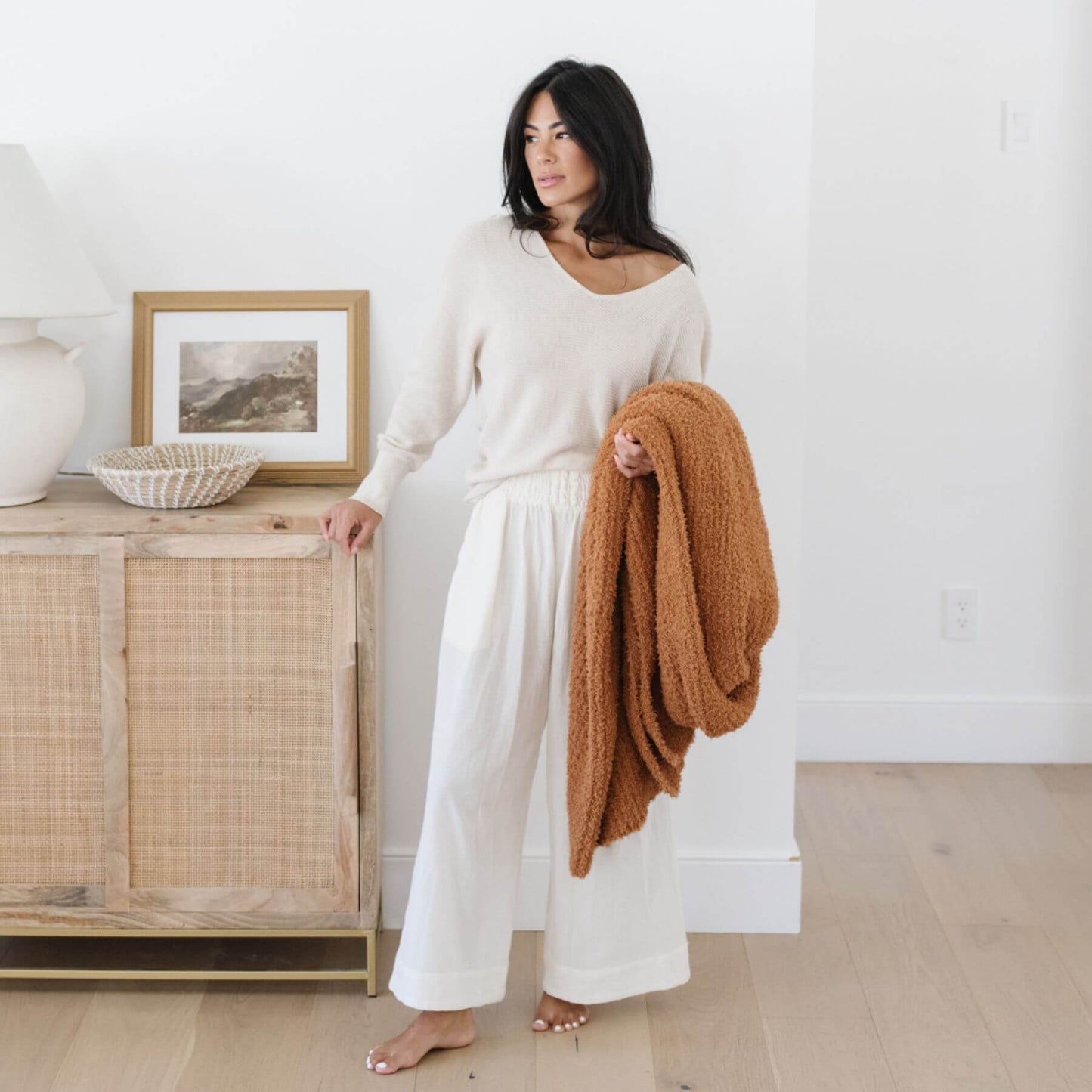 Woman in a white outfit holding Ribbed Bamboni® Throw Blankets Ginger in a minimalistic room.
