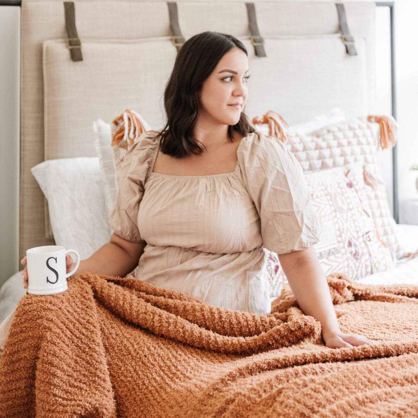 Woman sitting on a bed with Ribbed Bamboni® Throw Blankets Ginger and holding a mug.