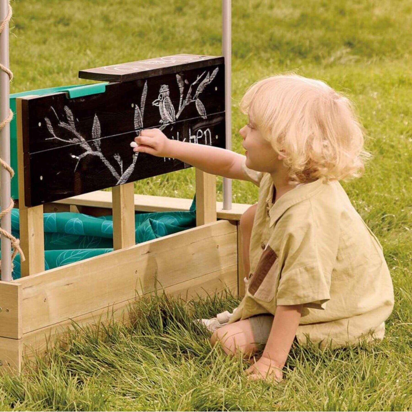Child drawing on a chalkboard of Hape Sandbox Cabana Kit in the background