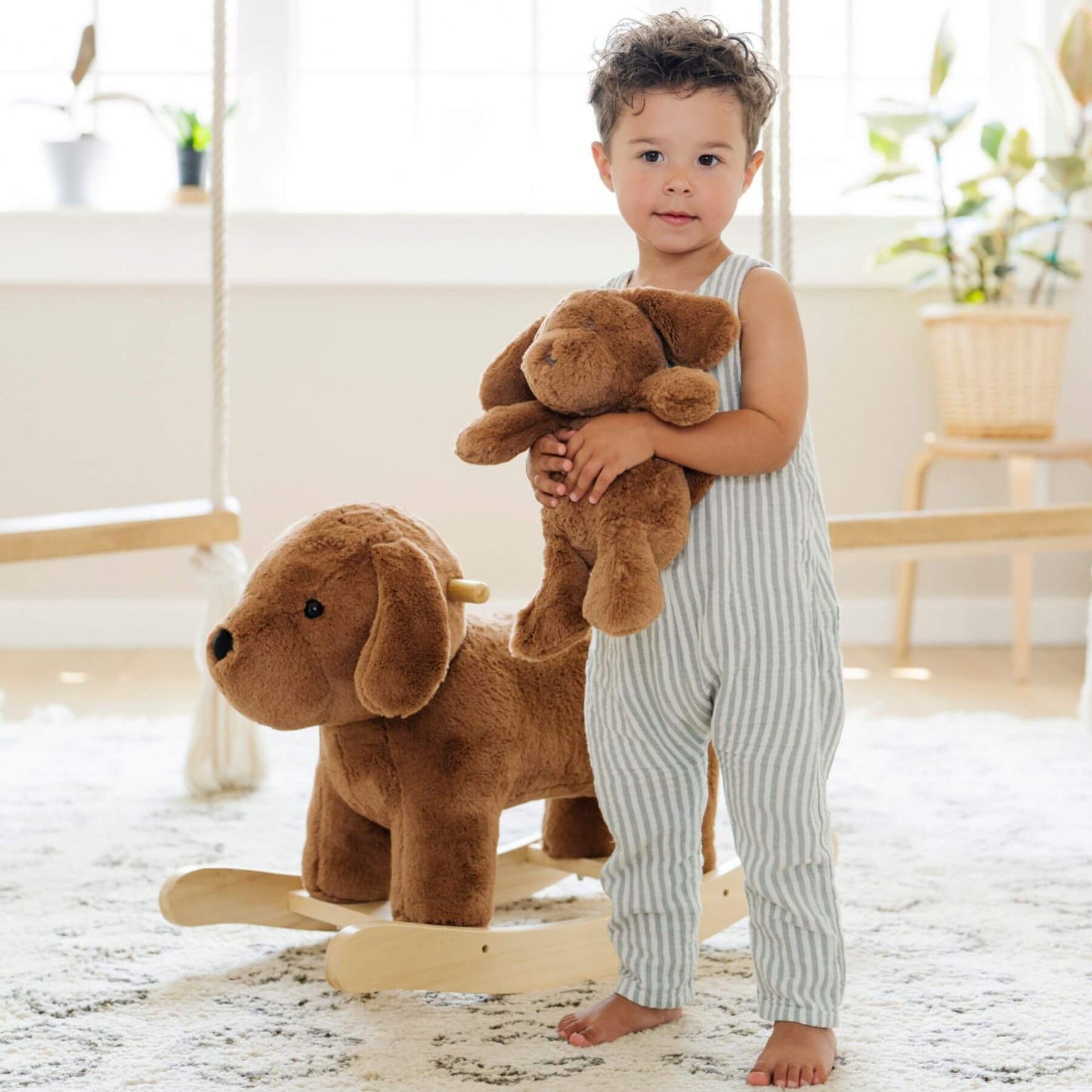 Child holding a teddy bear next to Saranoni Stuffed Animal Rocker - Dog in a bright room.