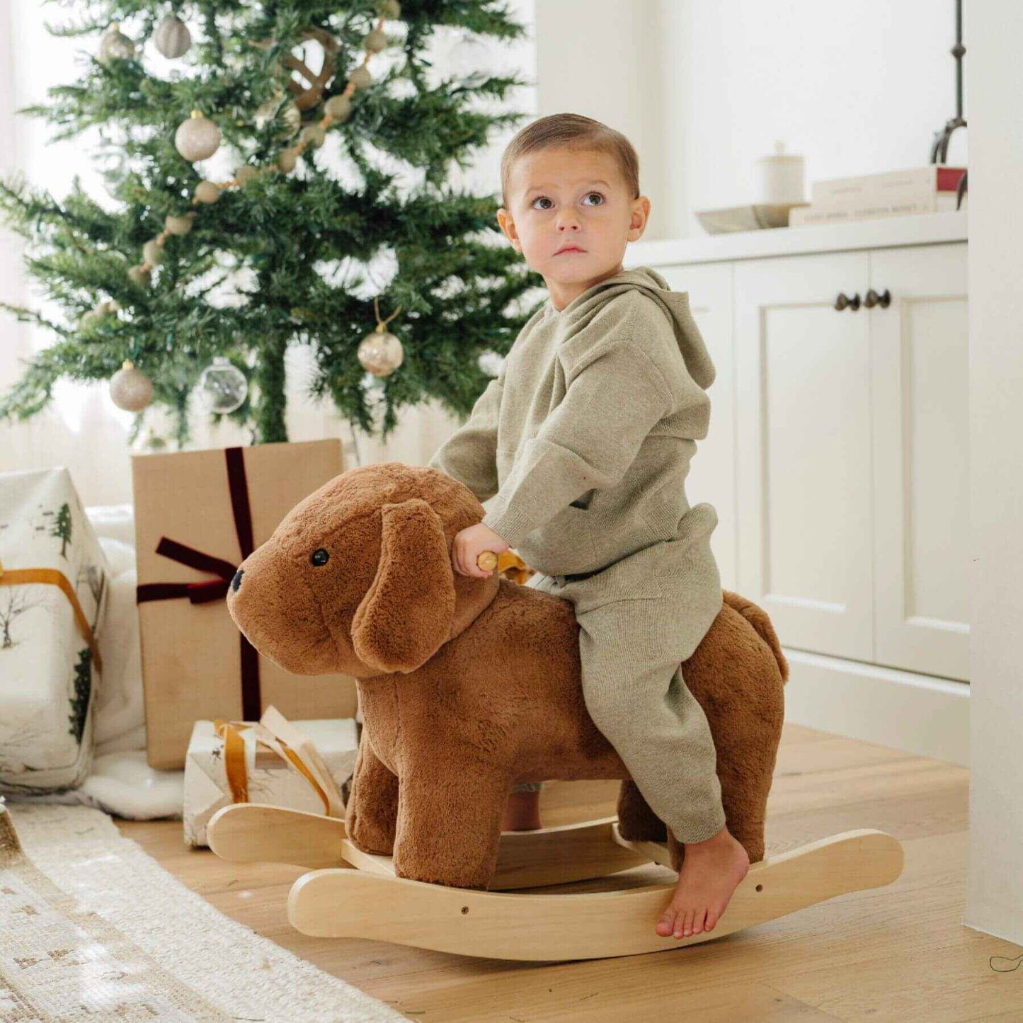 Child riding Saranoni Stuffed Animal Rocker - Dog in a room with a Christmas tree and presents.