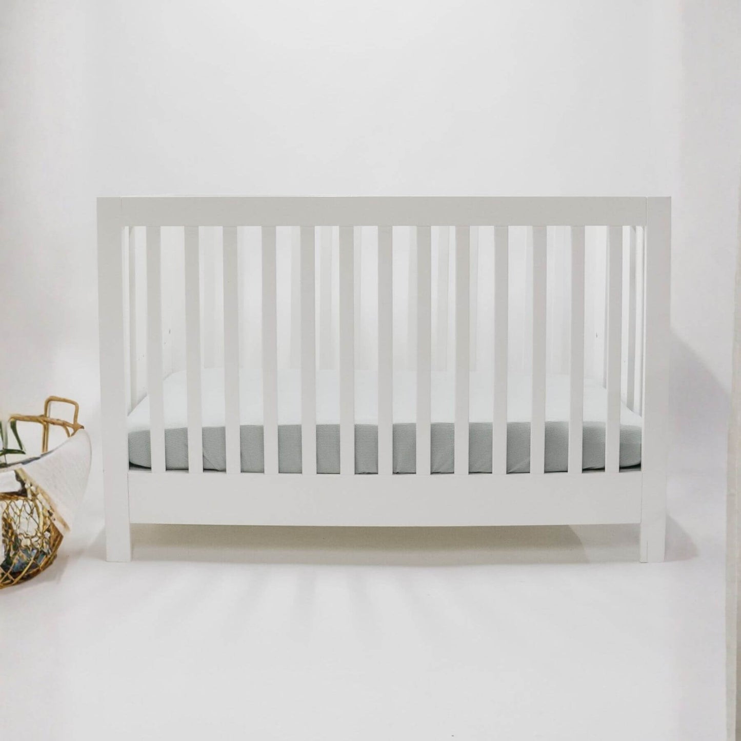 White crib with Little Mae & Co Seafoam Ribbed Crib Sheet against a white wall