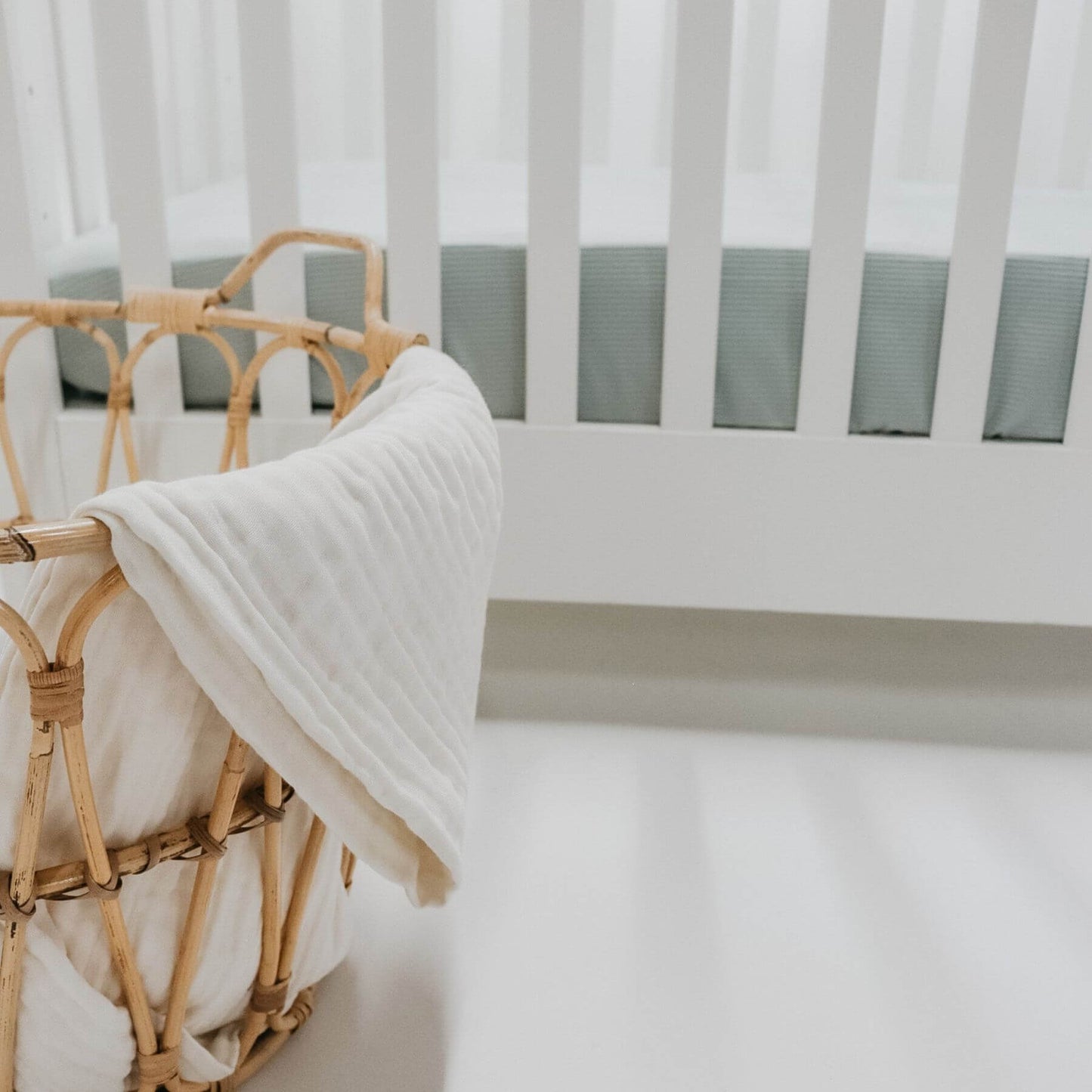 Bamboo basket with a crib and mattress covered with Little Mae & Co Seafoam Ribbed Crib Sheet