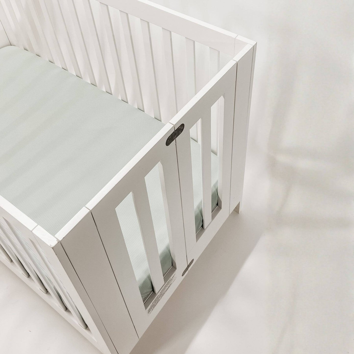 White crib with a mattress covered with Little Mae & Co Seafoam Ribbed Crib Sheet