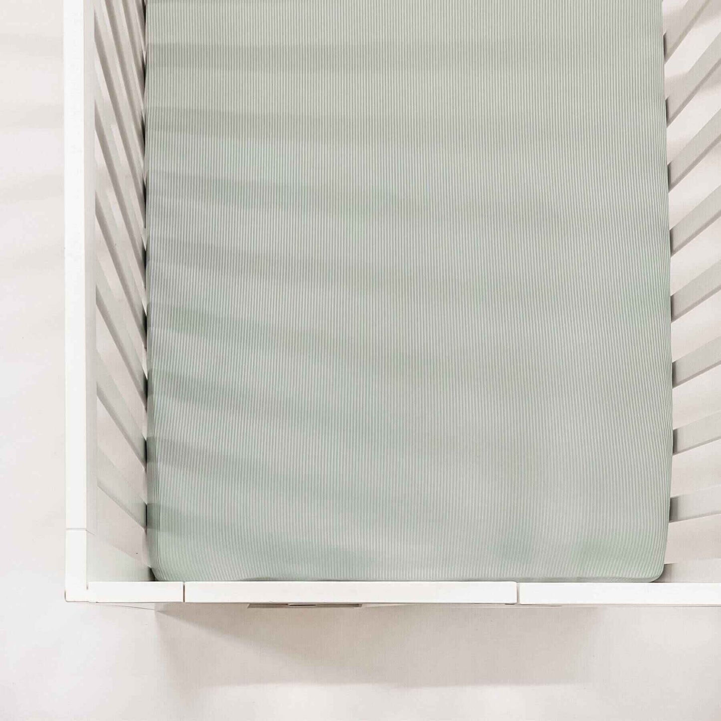 White crib with a mattress covered with Little Mae & Co Seafoam Ribbed Crib Sheet