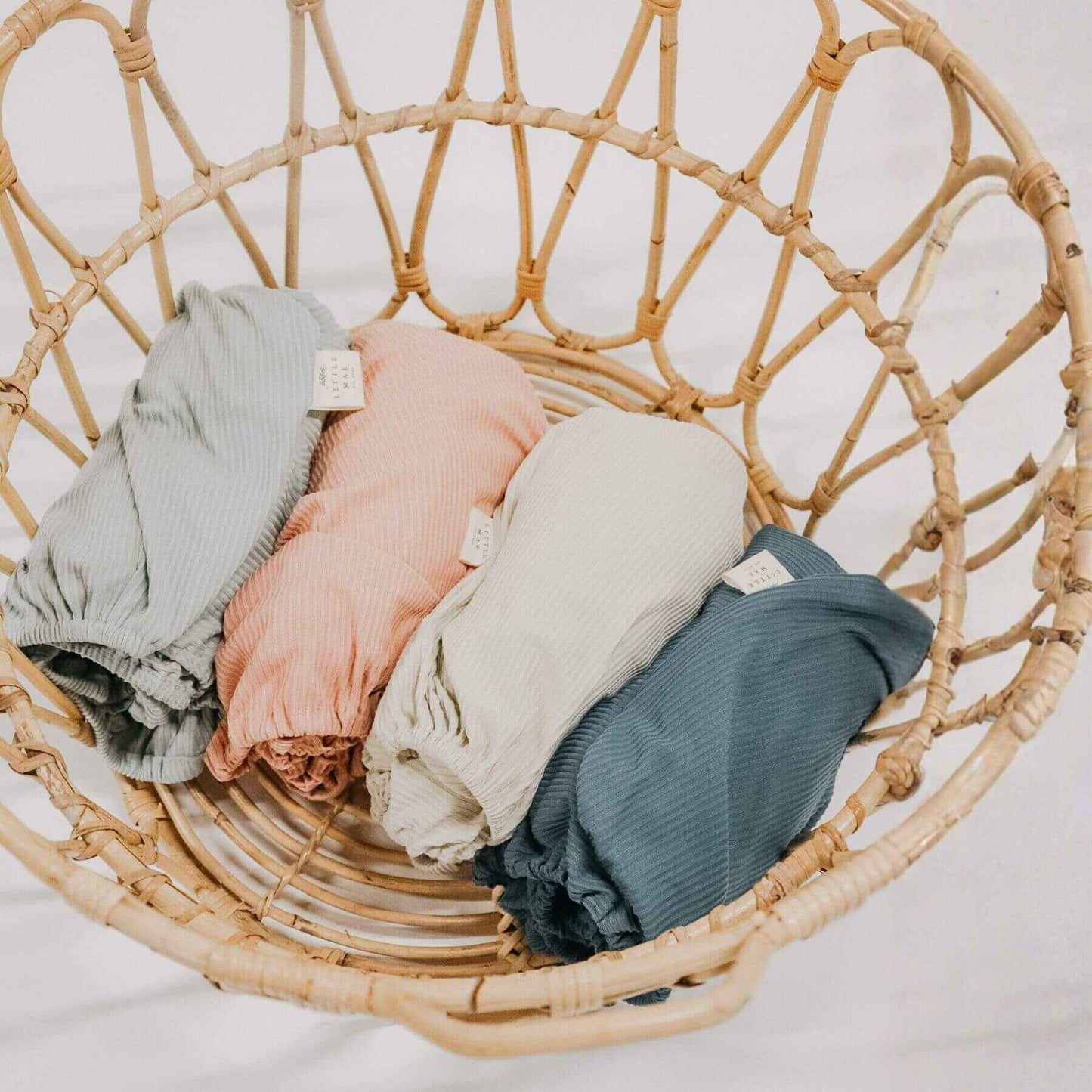 Folded Little Mae & Co Seafoam Ribbed Crib Sheets in a wicker basket on a light background