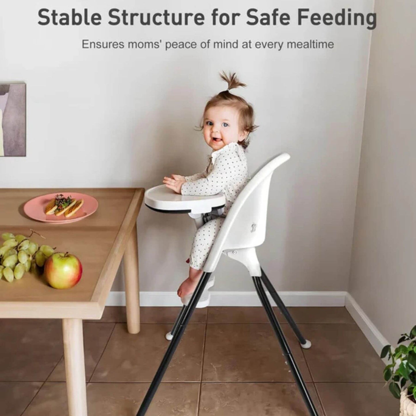 Child in SEGLONIA 3-in-1 Folding High Chair White/Black, surrounded by fruits on a table.