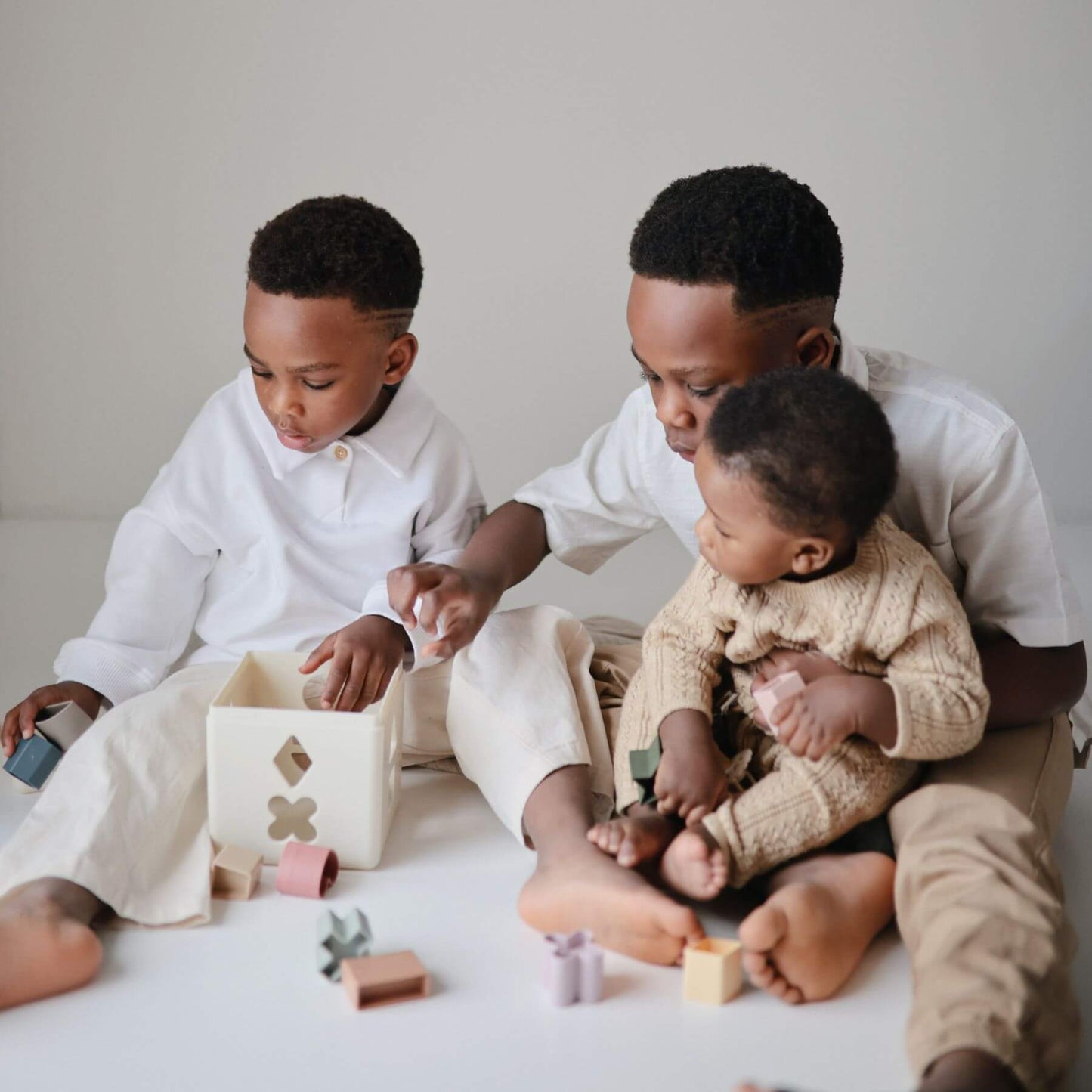 Man and two children playing together on a light-colored floor with Mushie Shape Sorting Box.