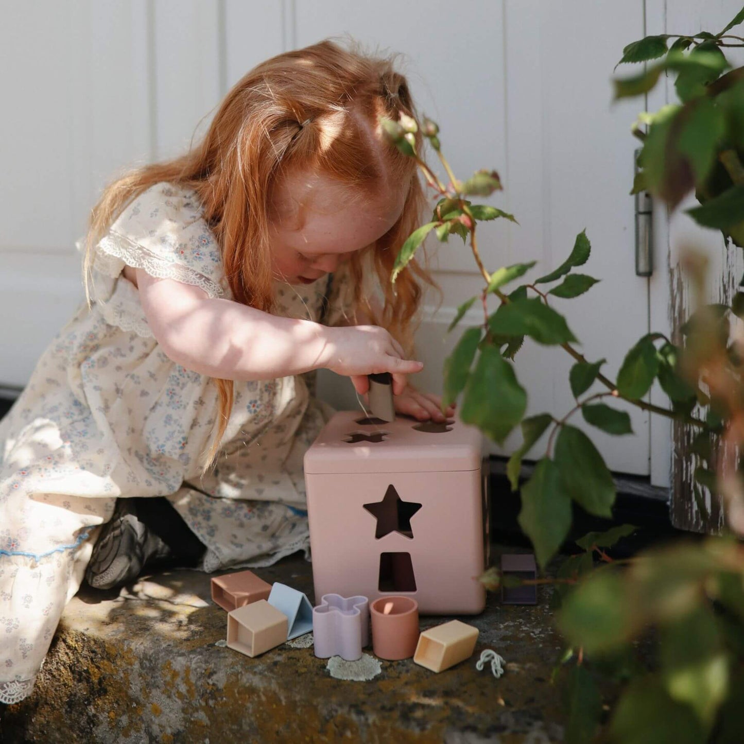 Child playing with Mushie Shape Sorting Box outdoors