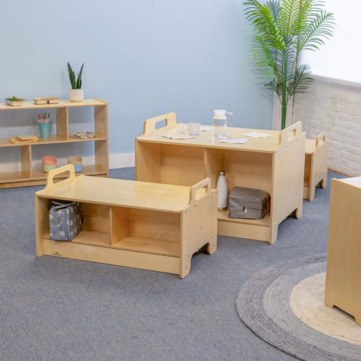 Children's wooden play furniture set in a room with a blue wall and plants.