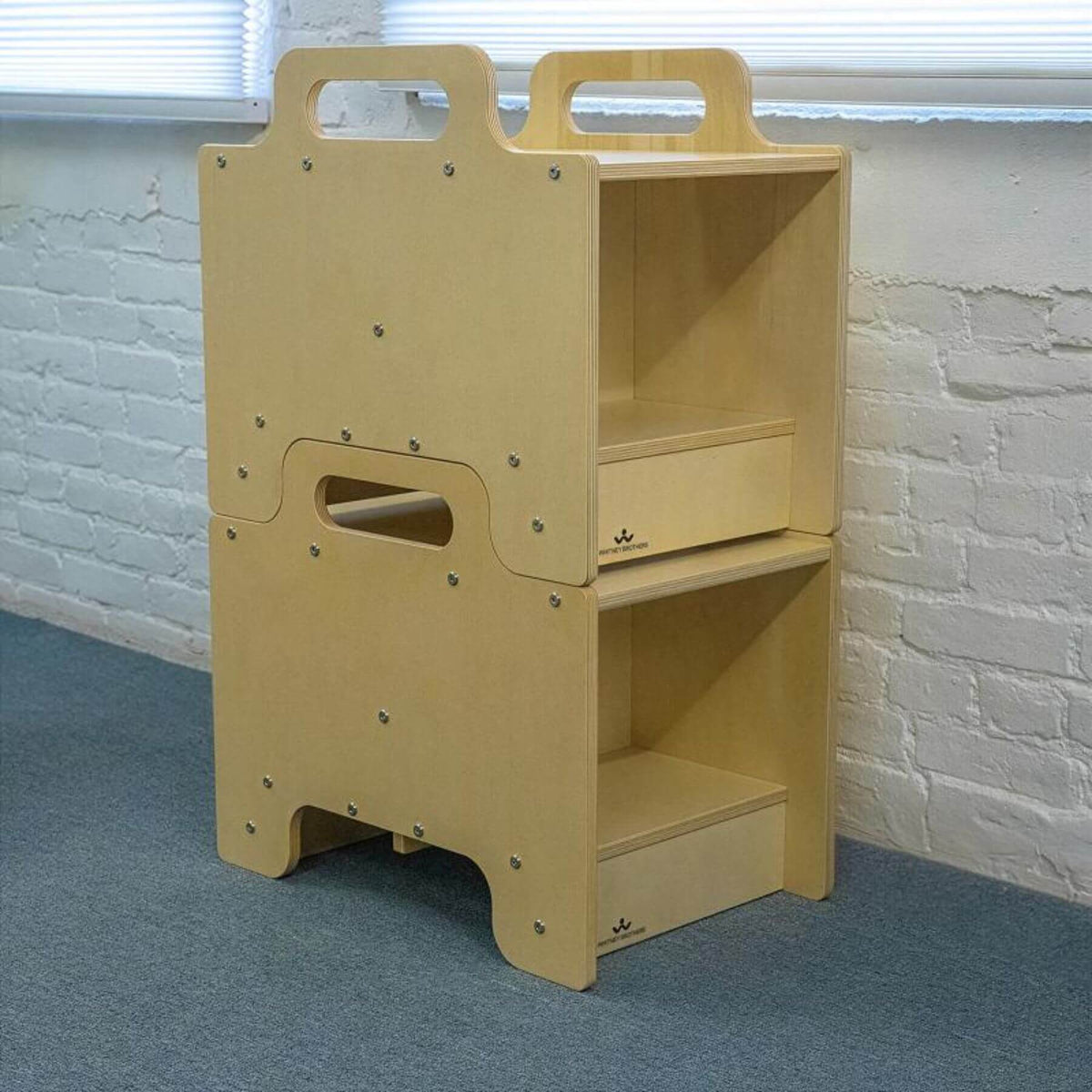 2 Whitney Brothers Stack-Able™ Seat against a white brick wall.