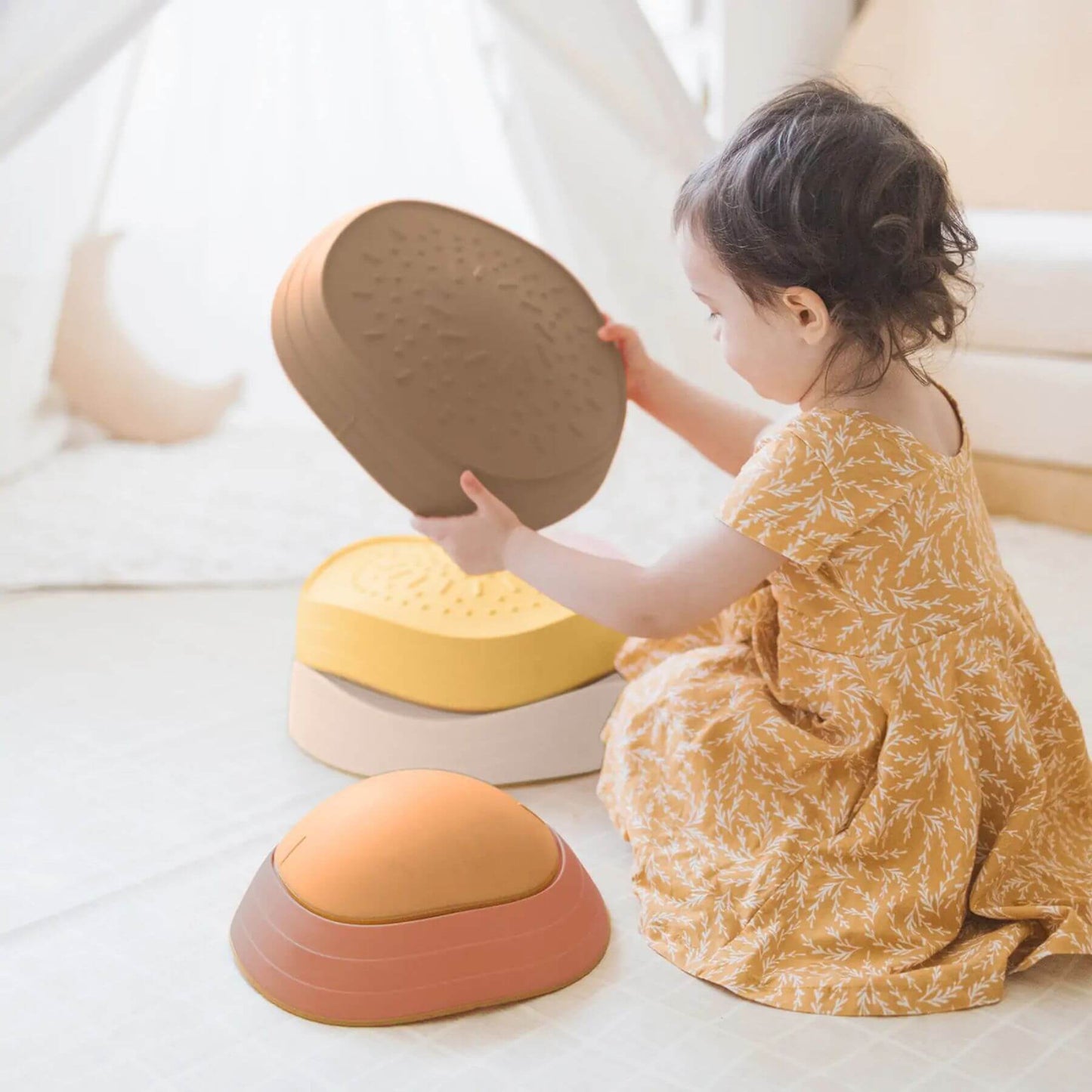Child playing with Tiny Land® Stepping Stones - Sunset Hues on a light-colored surface