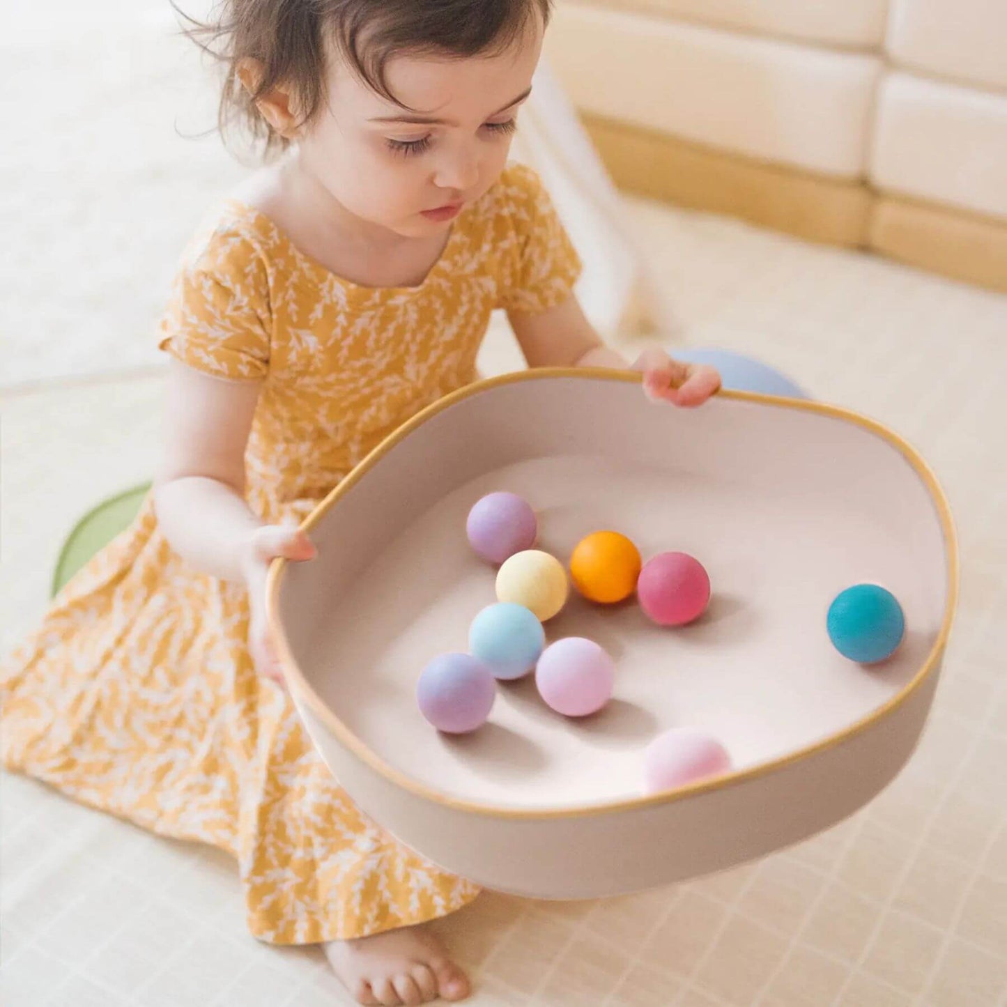 Child playing with colorful balls in Tiny Land® Stepping Stones on a light-colored floor.