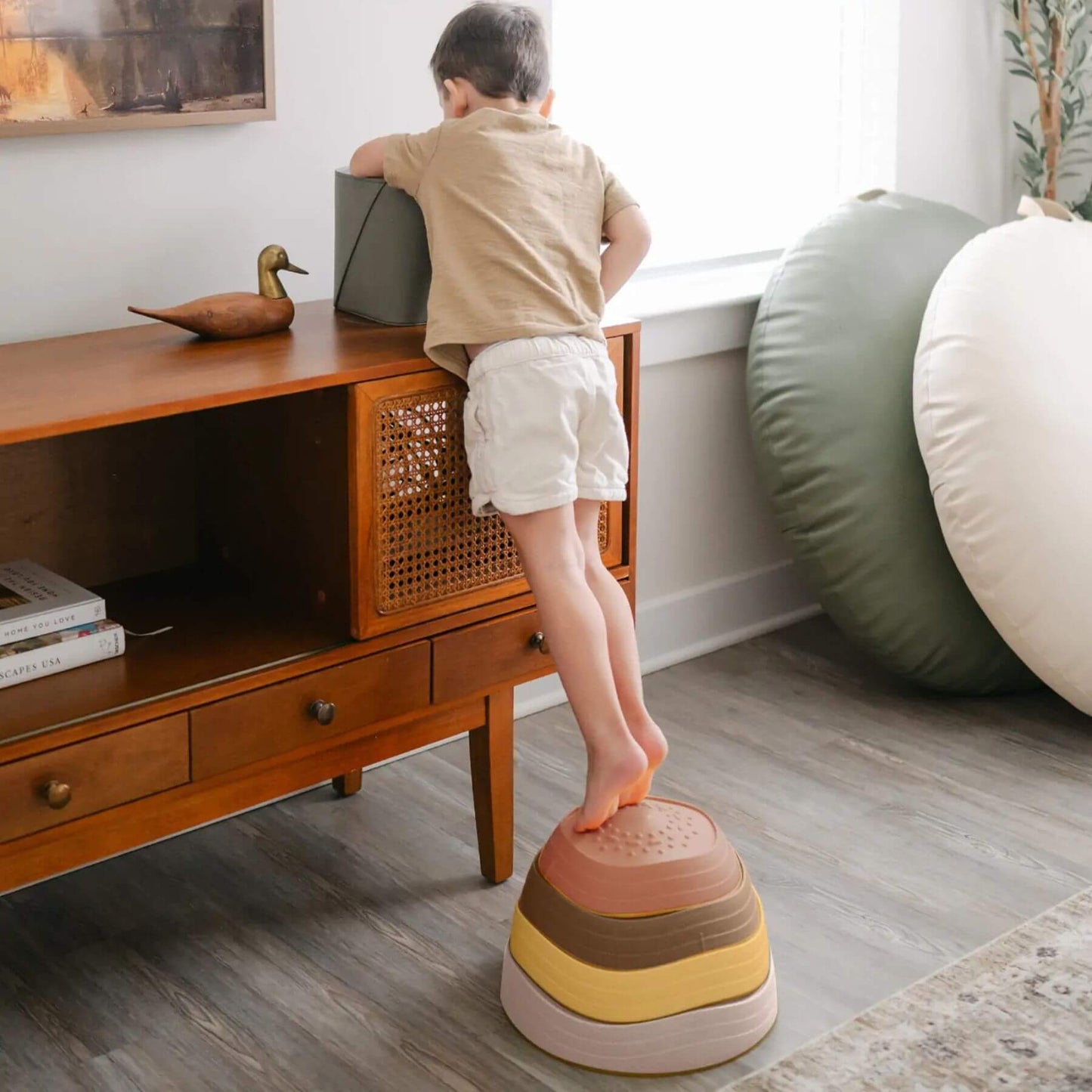 Child standing on Tiny Land® Stepping Stones - Sunset Hues in a room with wooden furniture and large cushions.