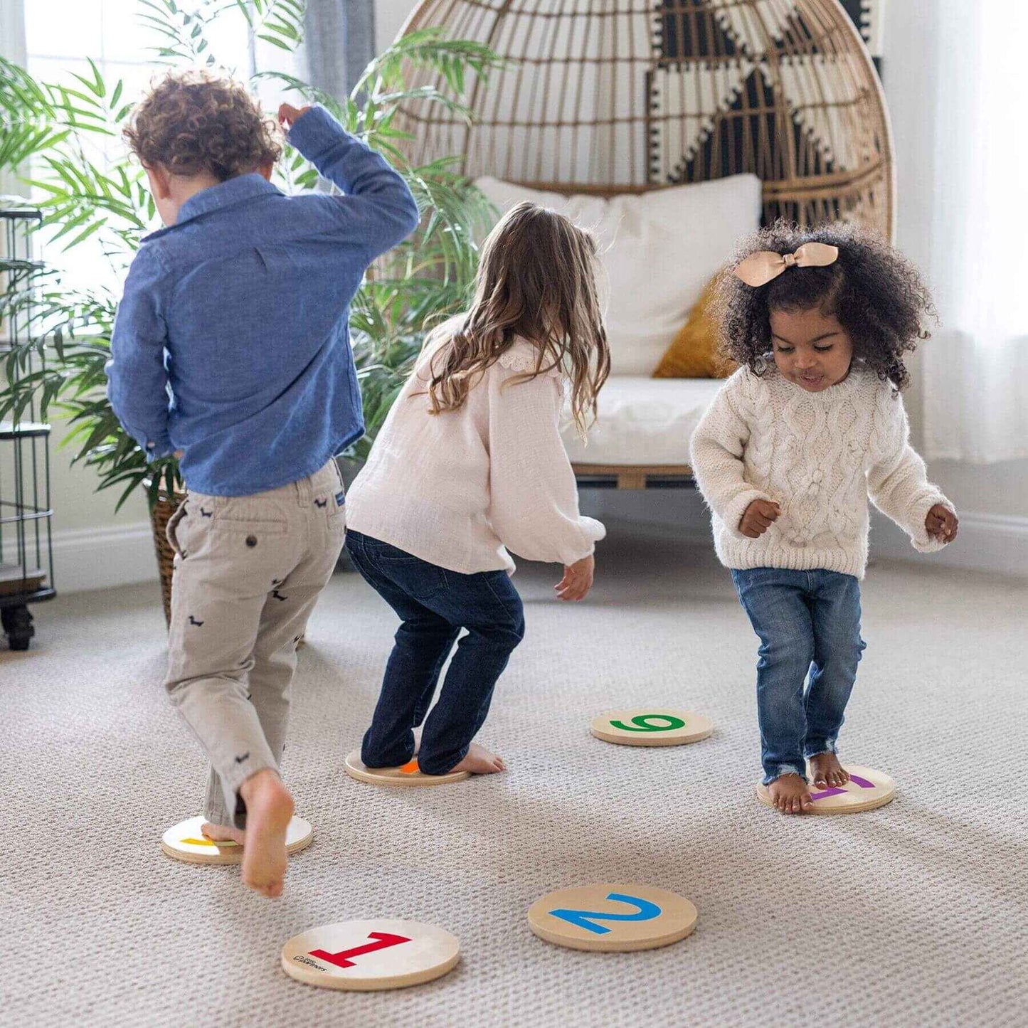 Three children playing with Little Partners Step 'N Learn Stepping Stones on a carpeted floor.