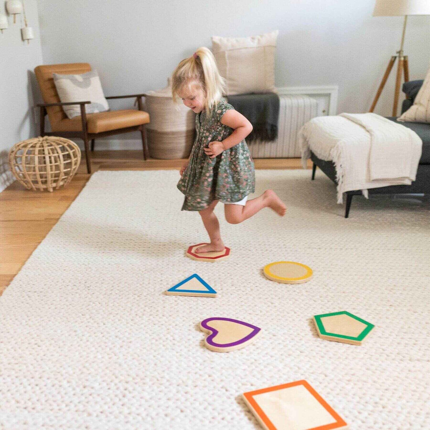 Child playing with Little Partners Step 'N Learn Stepping Stones Shapes on a textured floor in a living room.