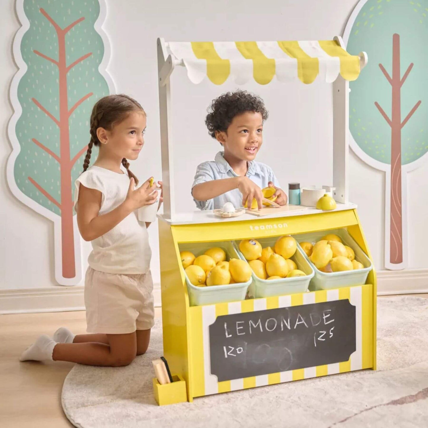Two children playing with Teamson Sunny Citrus Lemonade Stand Playset
