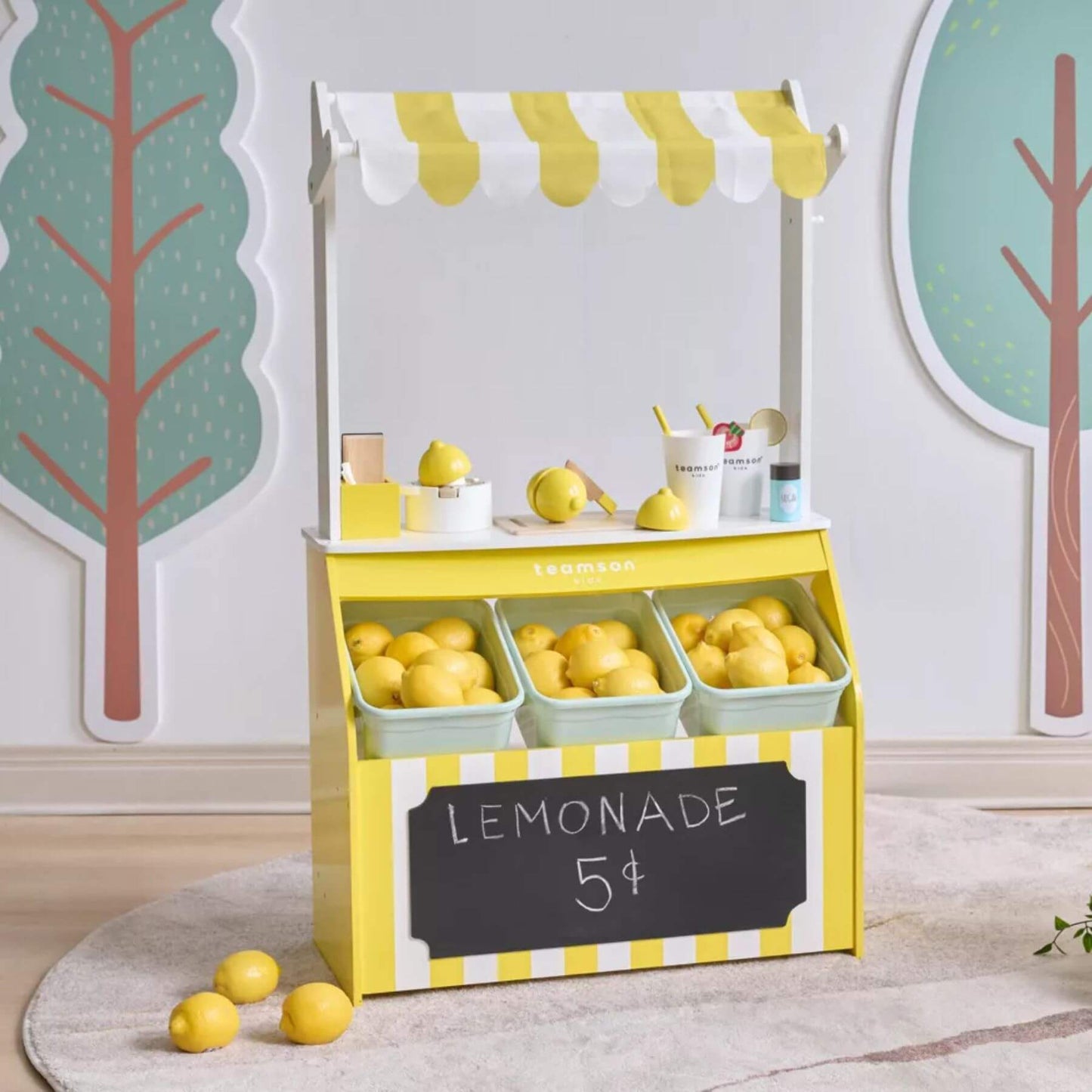 Teamson Sunny Citrus Lemonade Stand Playset with lemons and a chalkboard sign on a light gray floor.